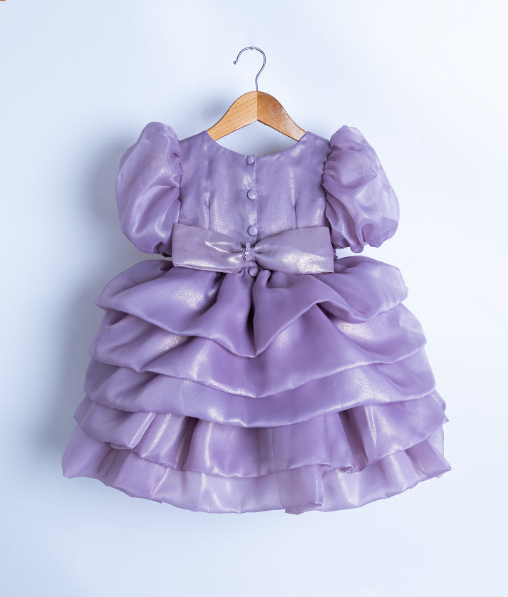 Back view of the lavender shimmer organza frock featuring a round neck, show button, and a large crystal-accented bow