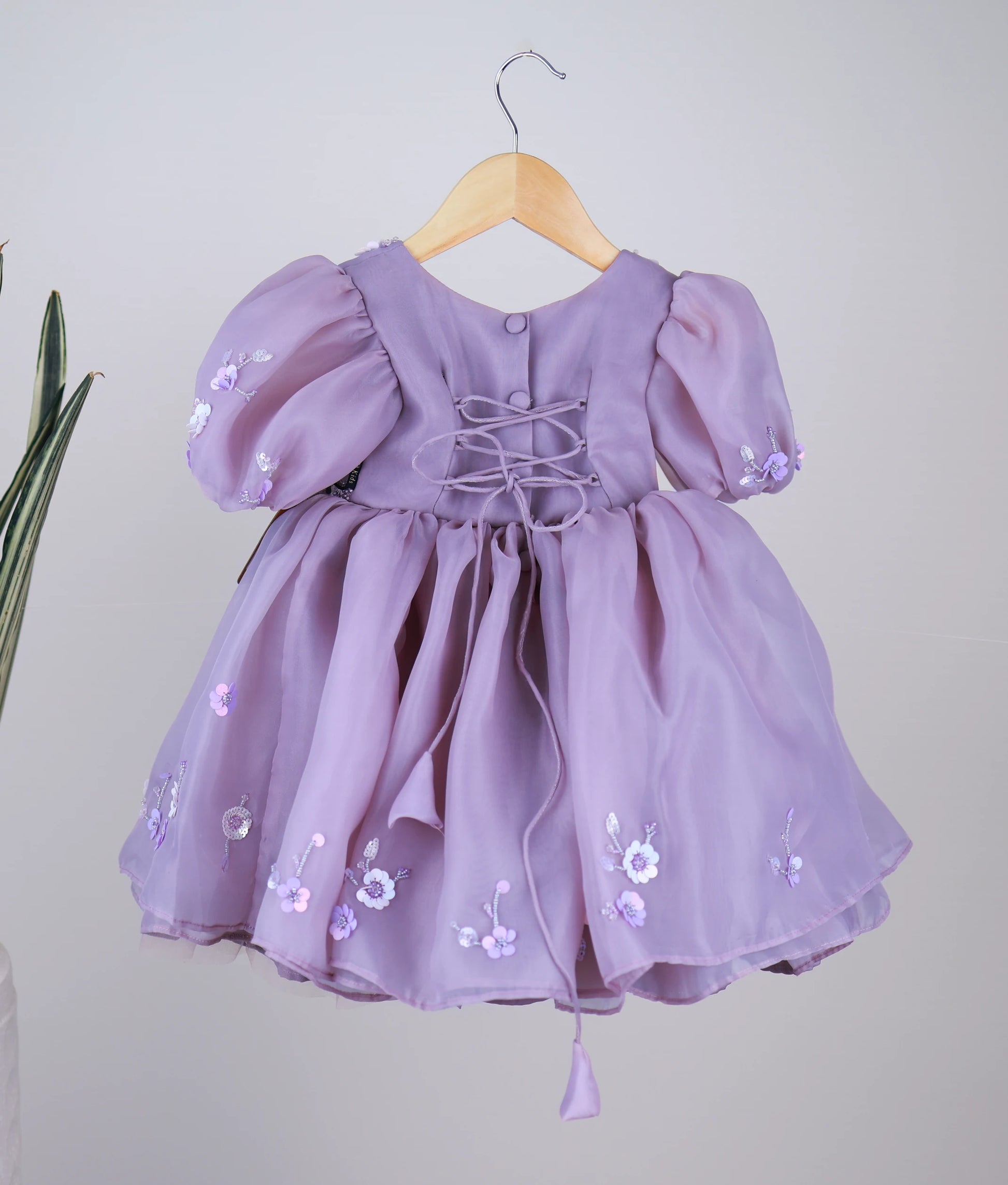 Back view of the lavender organza dress featuring a round neckline, show buttons, and a stylish cross-tie back