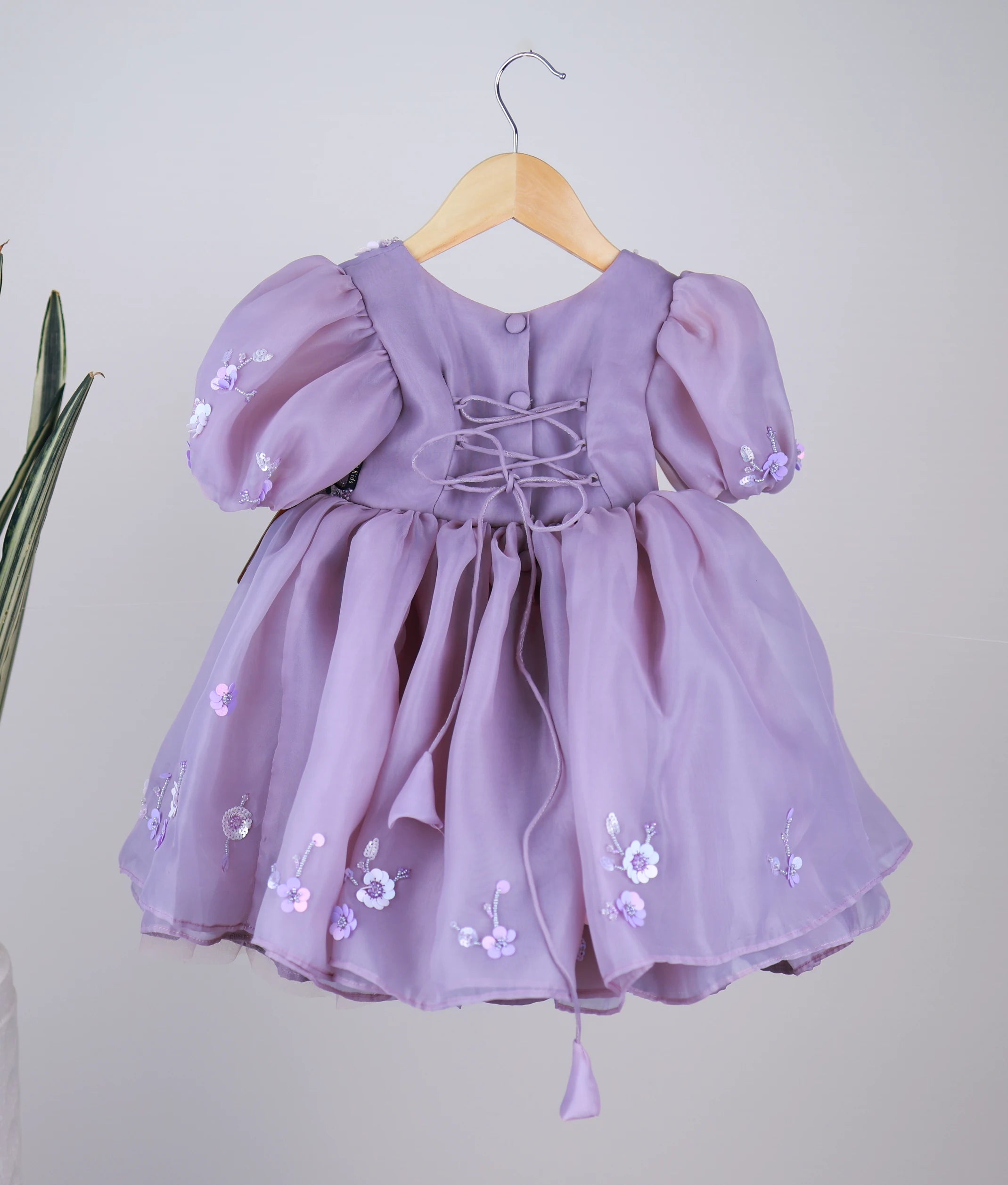 Back view of the lavender organza dress featuring a round neckline, show buttons, and a stylish cross-tie back