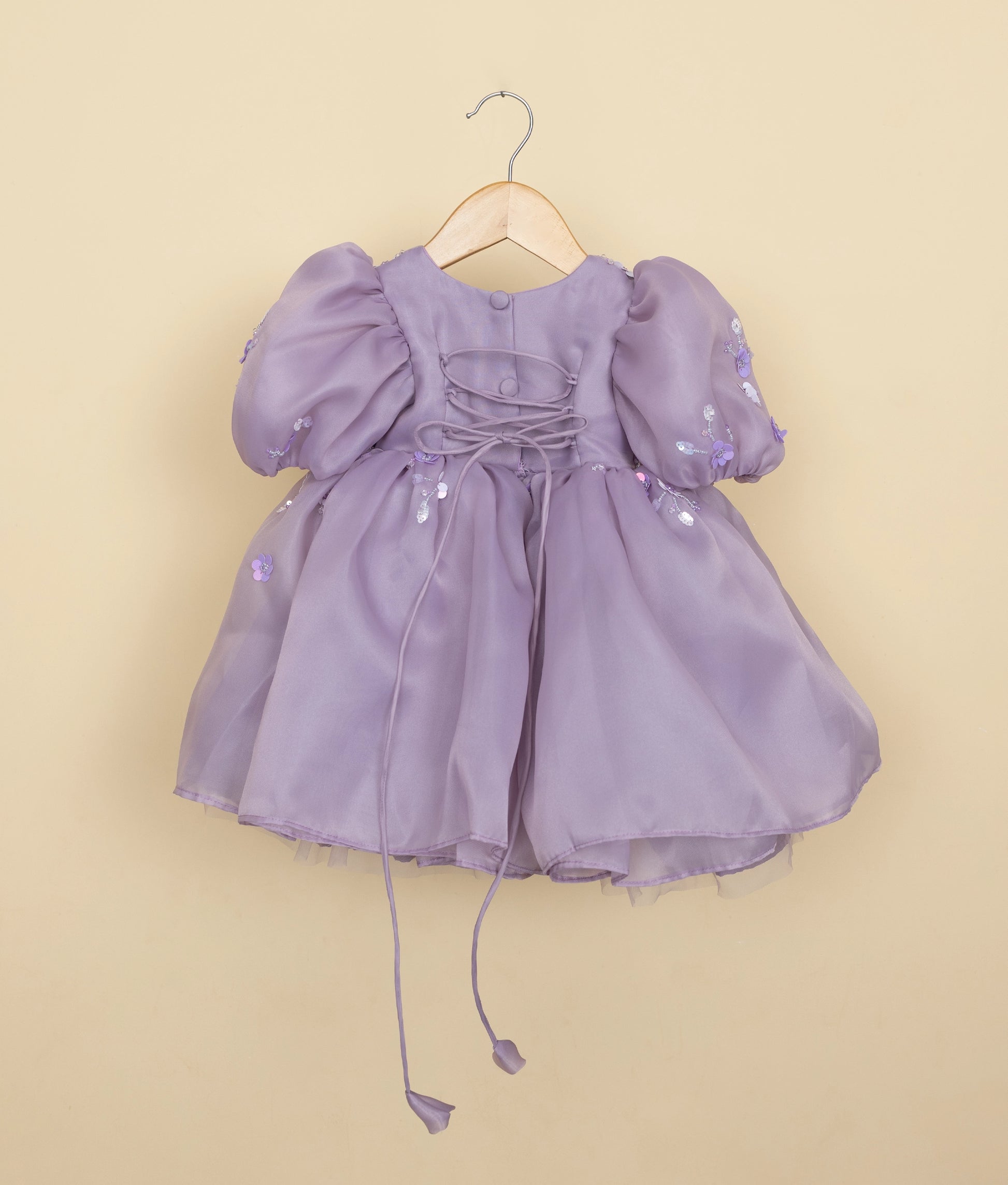 Back view of the lavender organza frock featuring a round neckline, show buttons, and a stylish cross-tie back