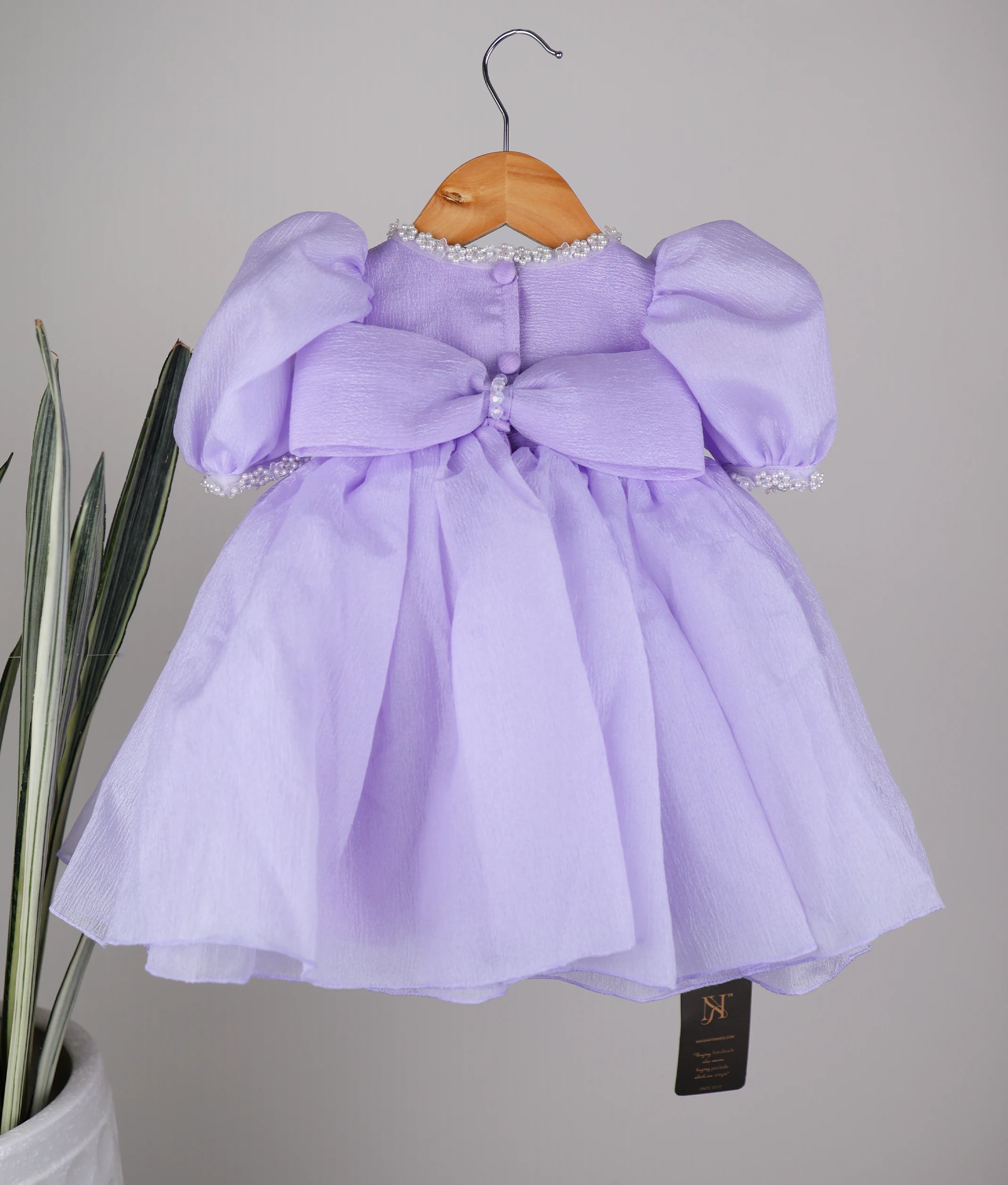 Back view of the lavender crush organza frock featuring a round neck, show button, and decorative bow detail