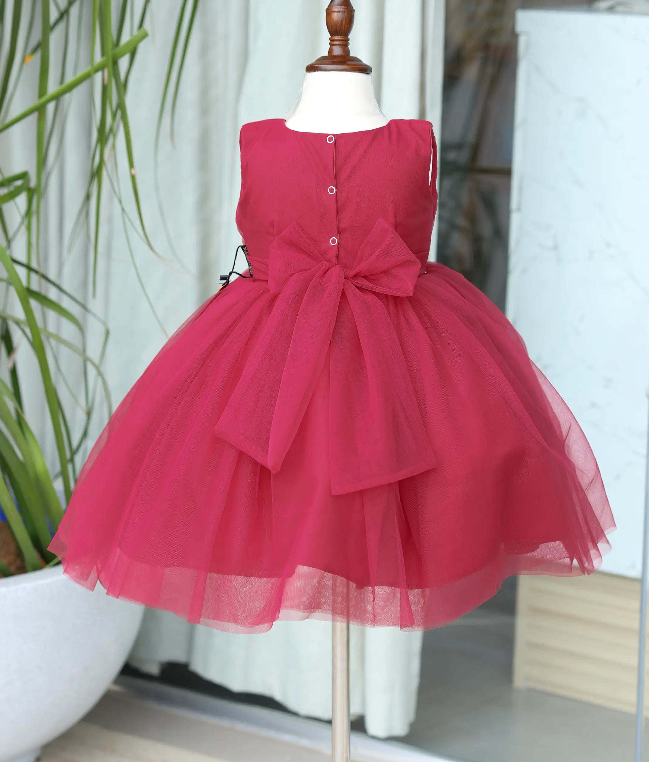 Back view of the ruby red frock showing the large net bow and button closure.