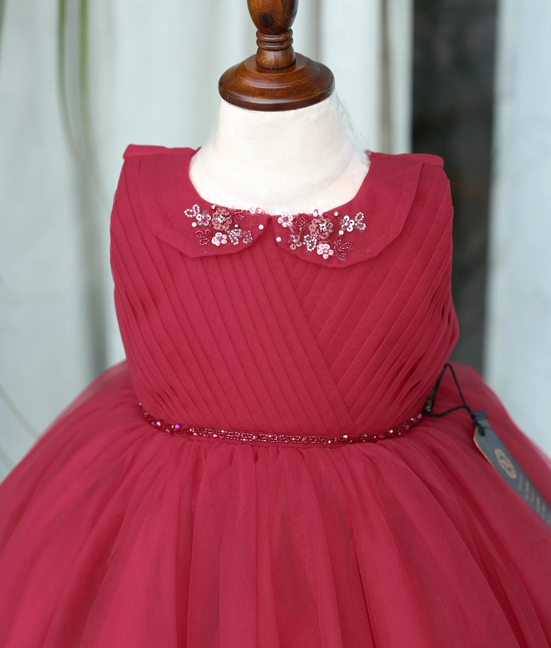 Close-up shot of the ruby red frock showing the floral handwork on the petal collar and the beaded belt.