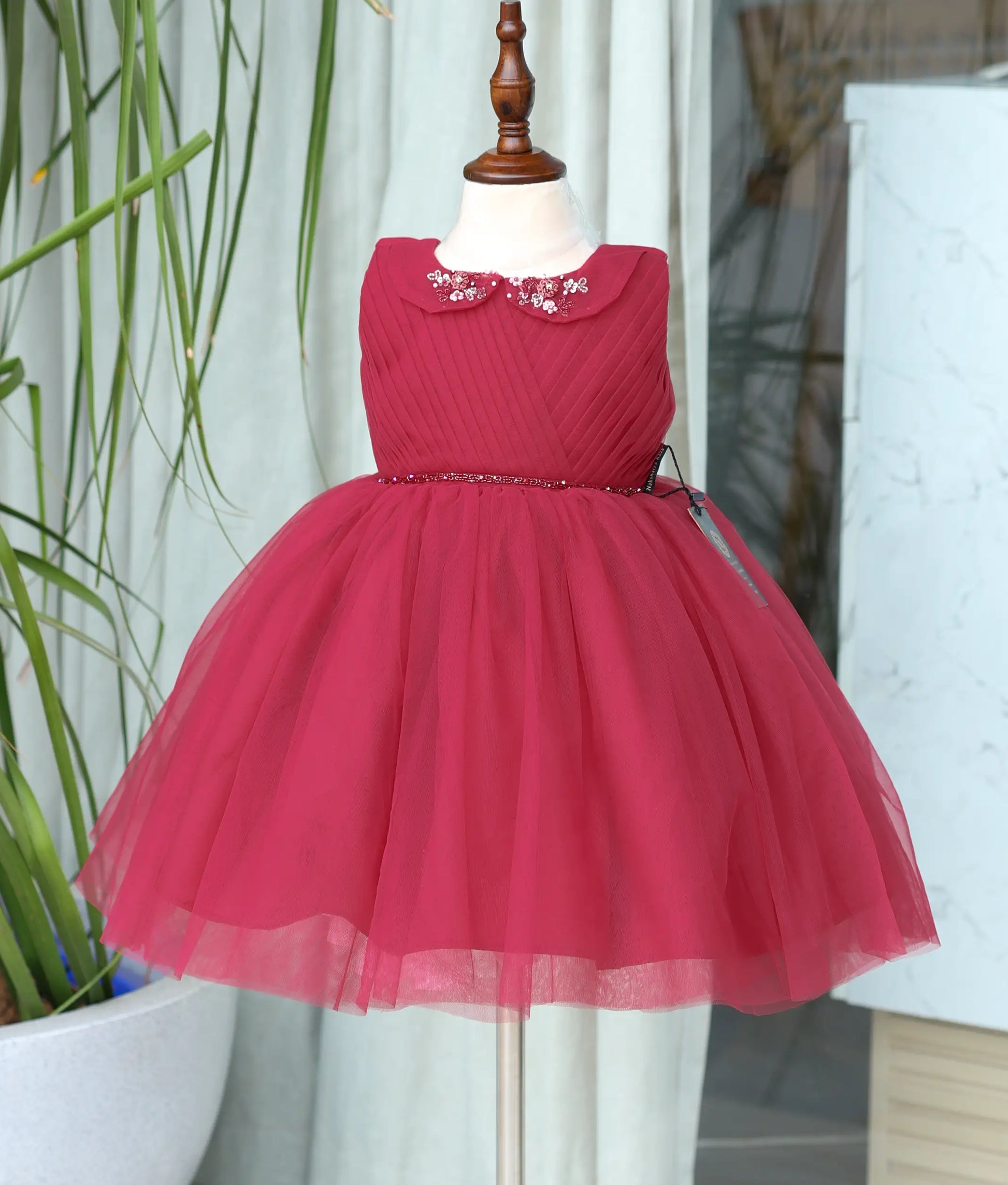 Front view of a ruby red party wear frock for girls with a pleated top and fluffy net bottom.