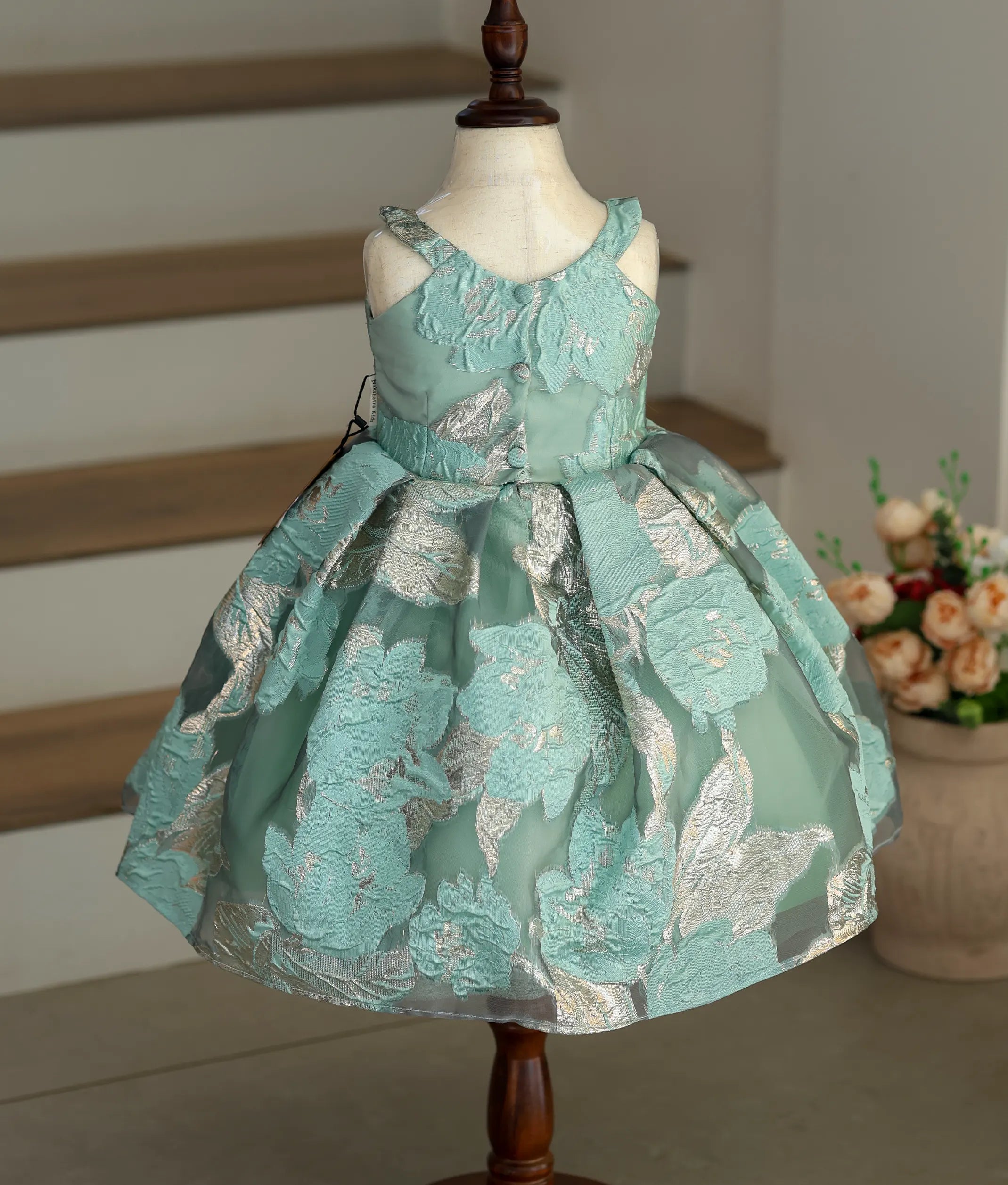Back view of the sea-green frock showing the pleated flair and button closure.