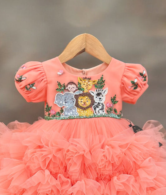 Close view of a coral orange baby girl birthday dress with puff sleeves, sequin jungle animal embroidery on the bodice, and a layered ruffled tulle skirt.
