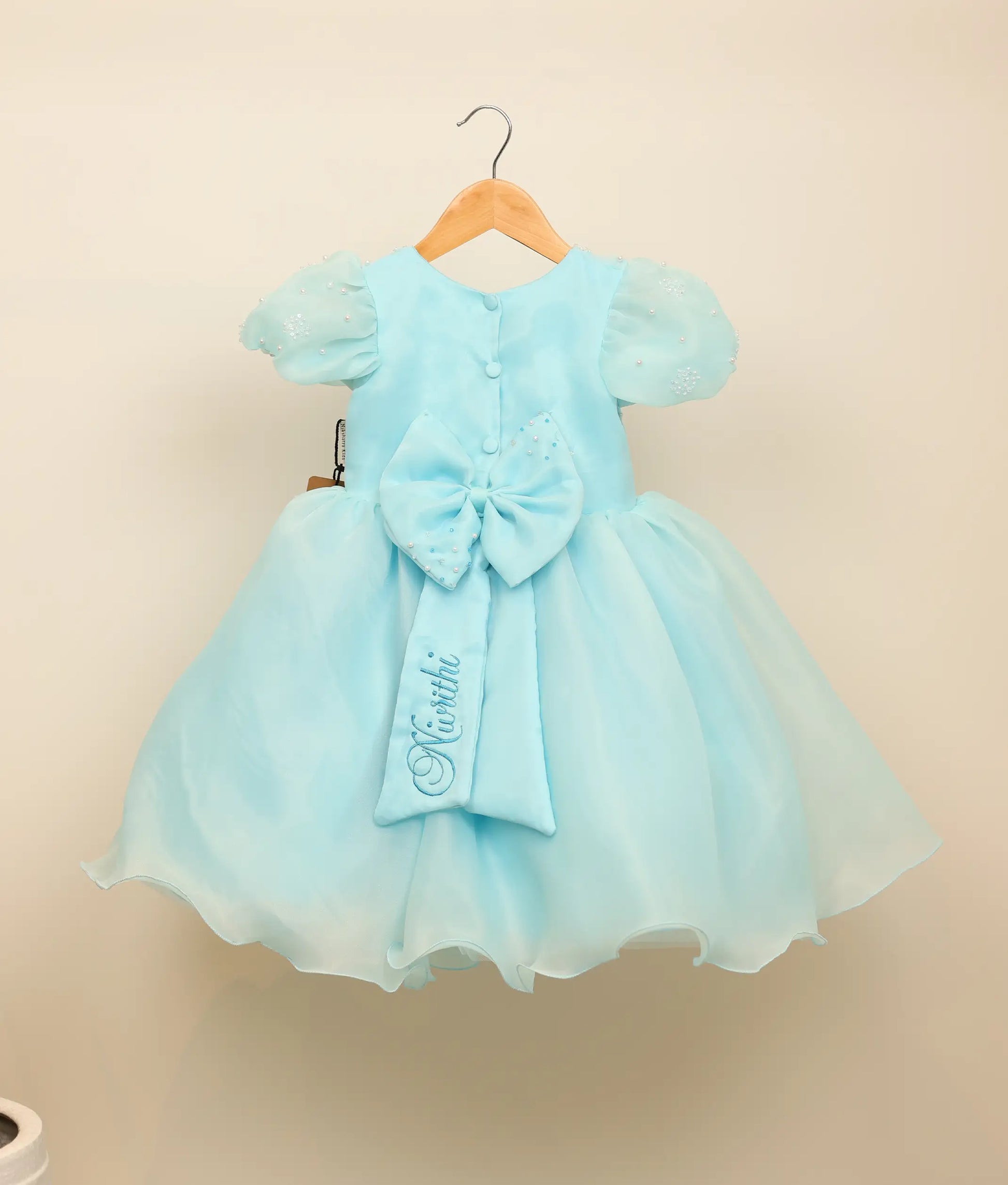 Back view of the sky blue Baby Shark frock showing the round neck, show button, and decorative bow with tie