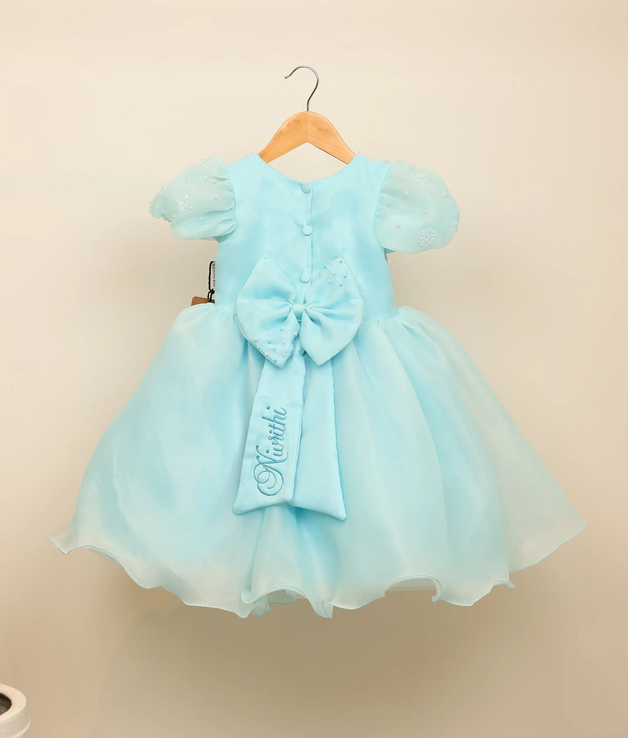 Back view of the sky blue Baby Shark frock showing the round neck, show button, and decorative bow with tie