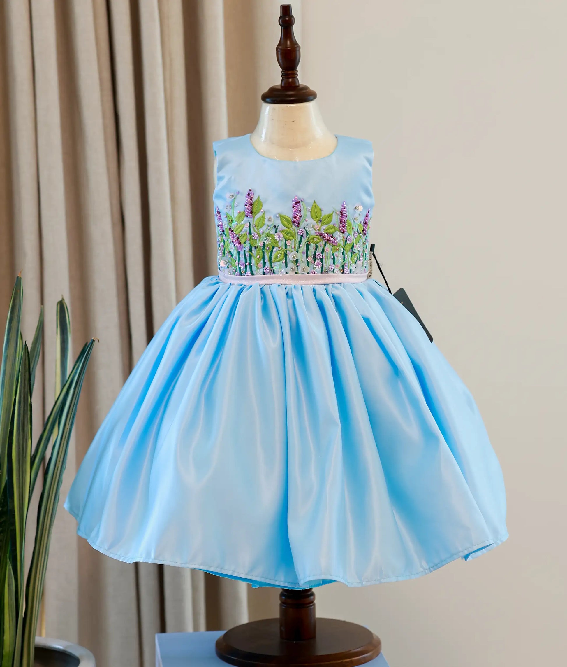 Front view of a sky blue bridal satin organza flower theme dress for baby girls featuring a sleeveless handworked yoke and layered skirt