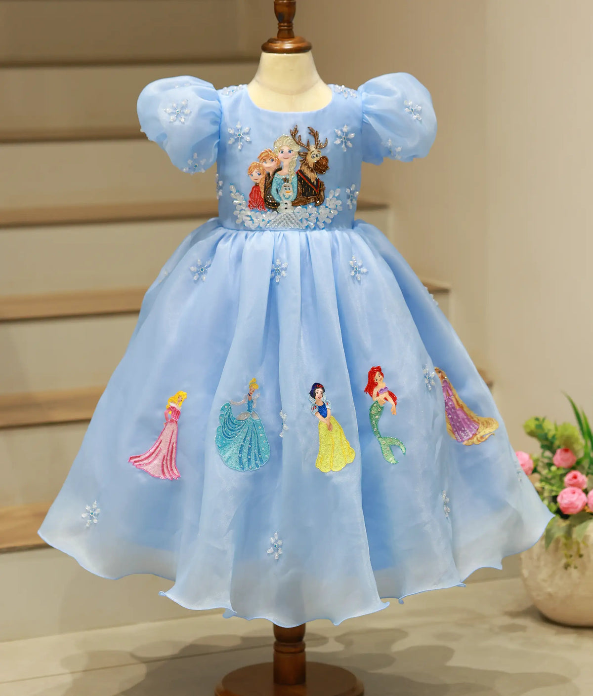 Front view of sky blue organza gown featuring hand-painted Elsa and friends on the skirt on mannequin.