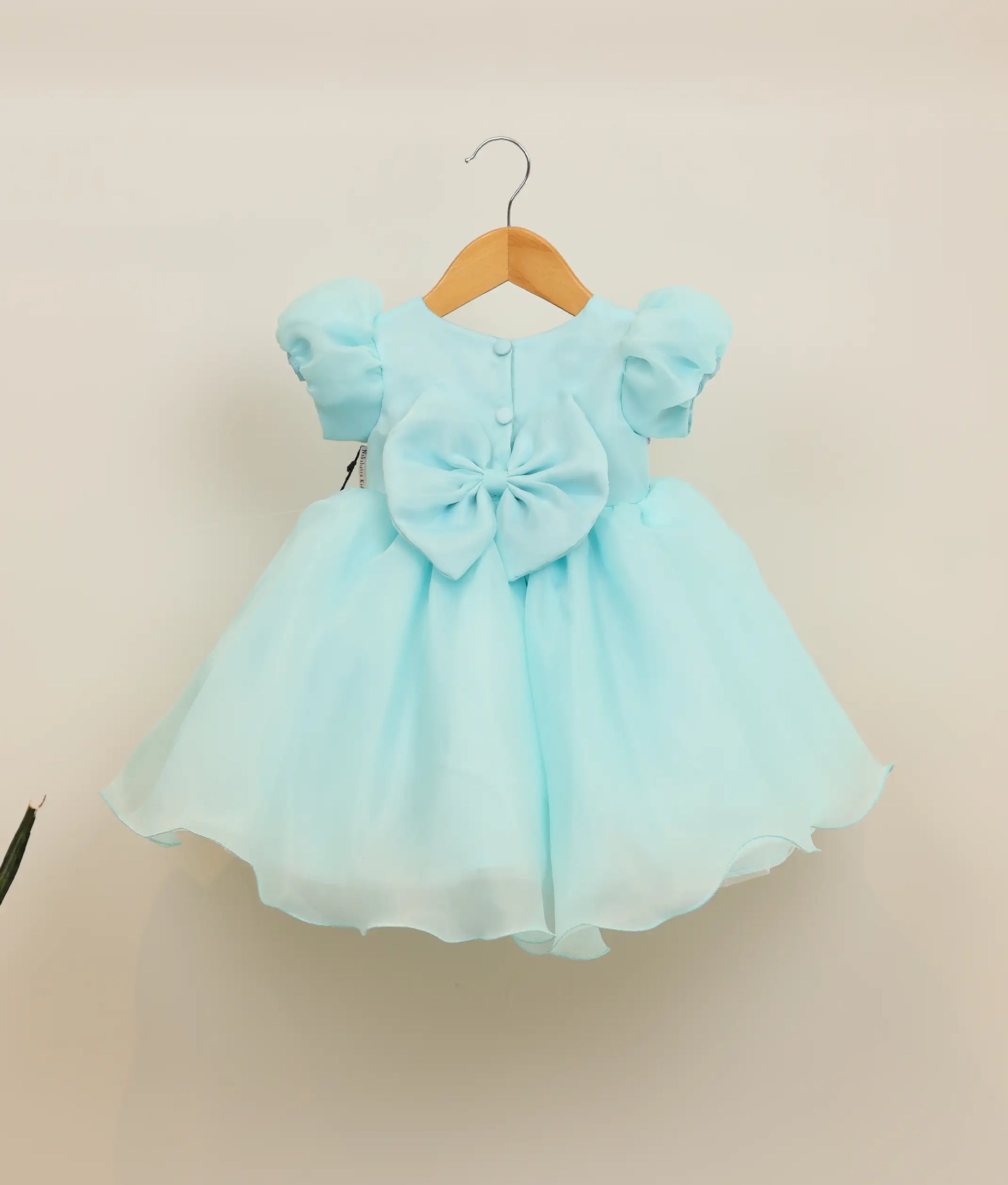 Back view of sky blue organza dress showing the round neck with show button, back bow, and voluminous flowy skirt