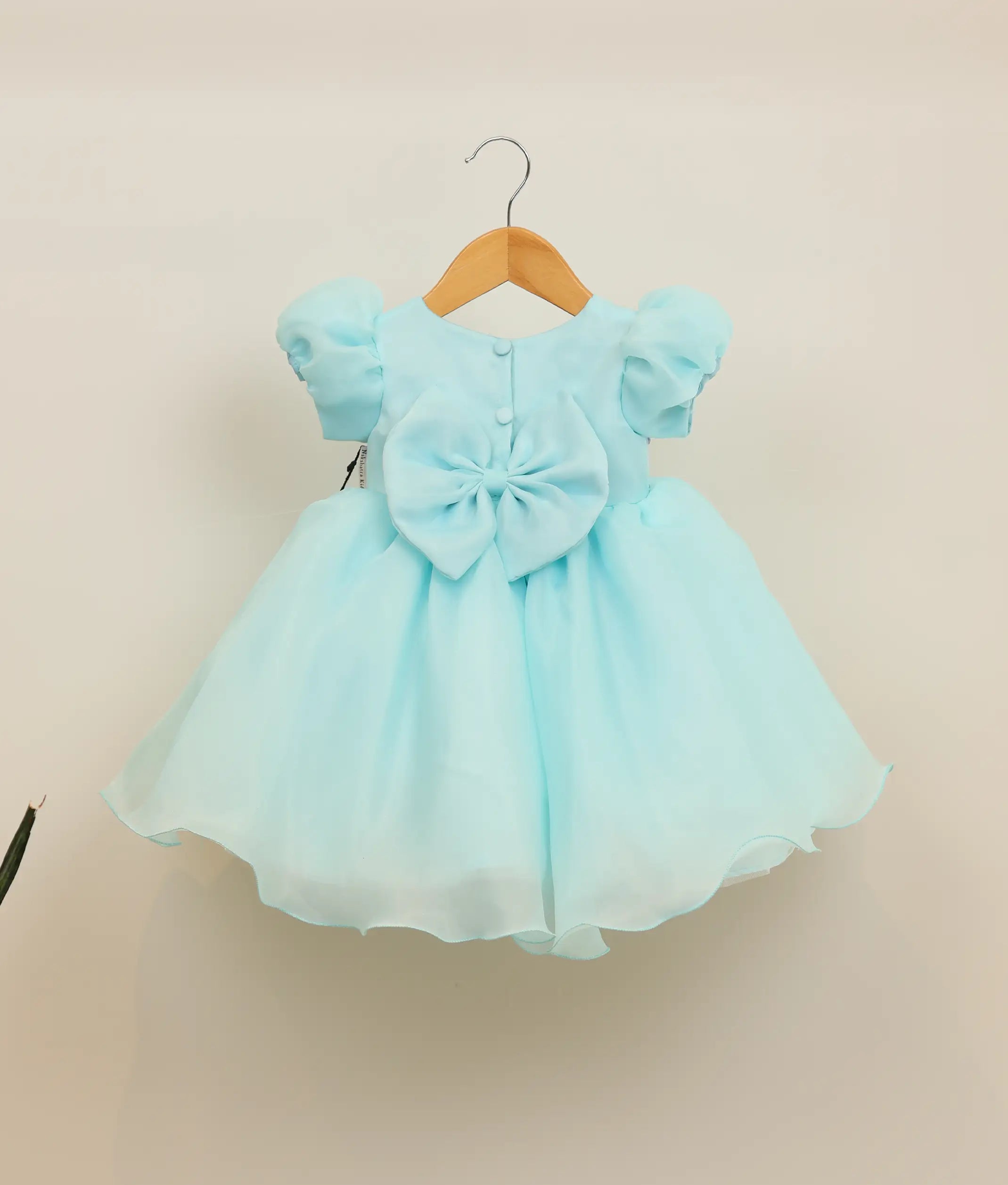 Back view of sky blue organza dress showing the round neck with show button, back bow, and voluminous flowy skirt
