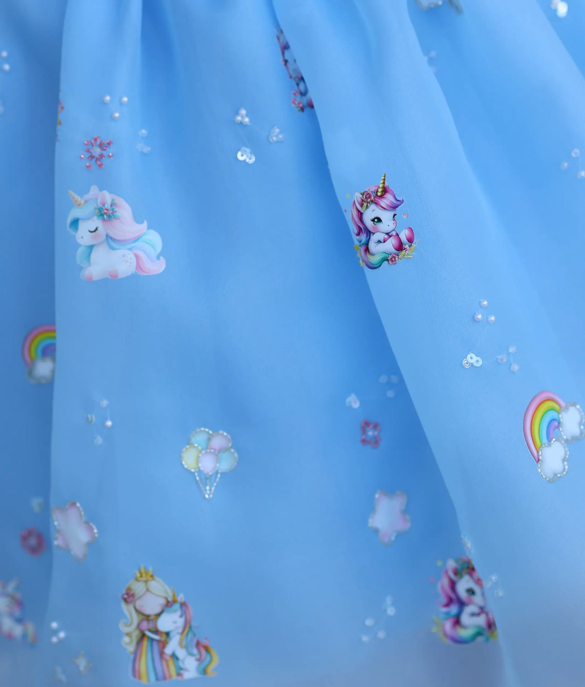 Close-up of hand-embroidered unicorn and balloon motifs on baby girl's sky blue party frock