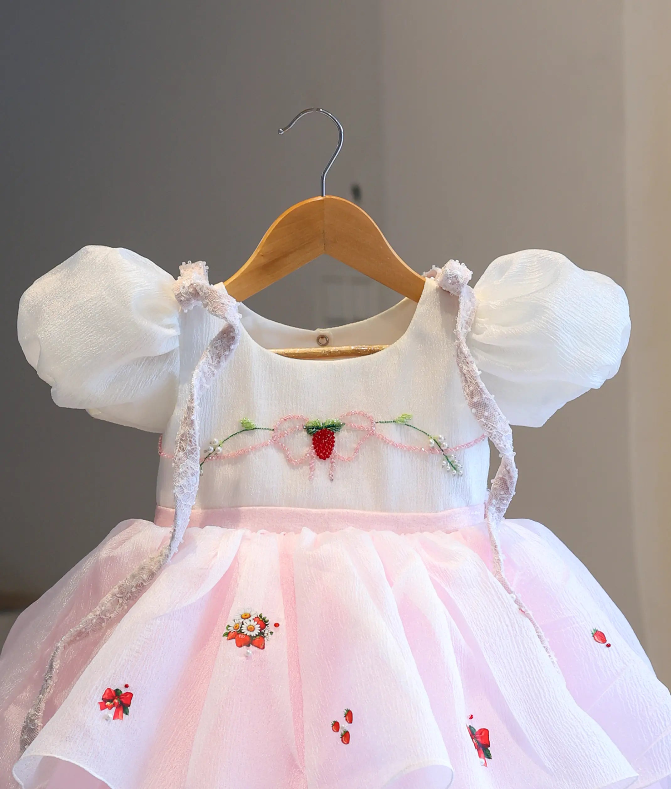 Close-up detail of the white bodice, showcasing the hand-embroidered strawberry, pink beadwork bow, shoulder lace trim, and strawberry print details on the skirt.