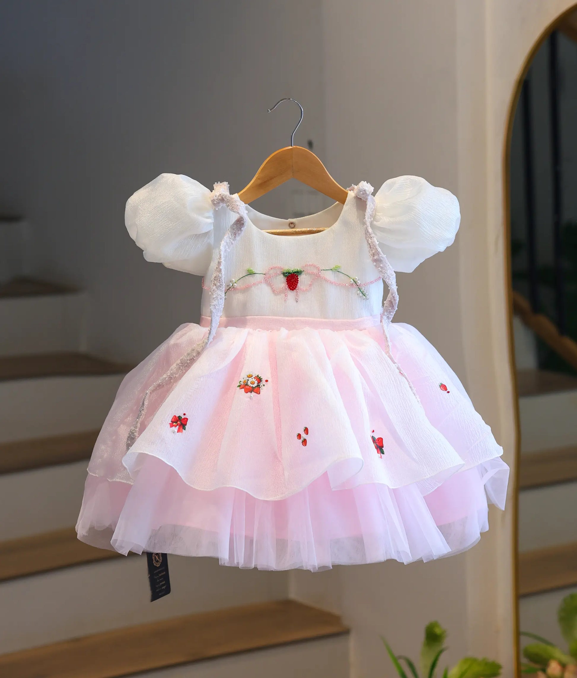 Full-length front view of the strawberry-themed kids party dress hanging up, highlighting the white puff-sleeve top and the tiered baby pink crush organza and tulle net skirt.