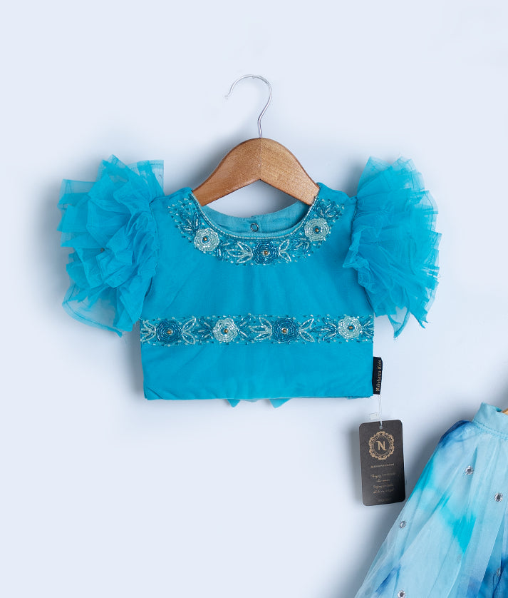 Close-up of turquoise baby dress top with feathered sleeves and floral embellishments