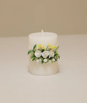 White pillar baptism candle decorated with yellow silk flowers, white lace ruffles, and gold pearl accents