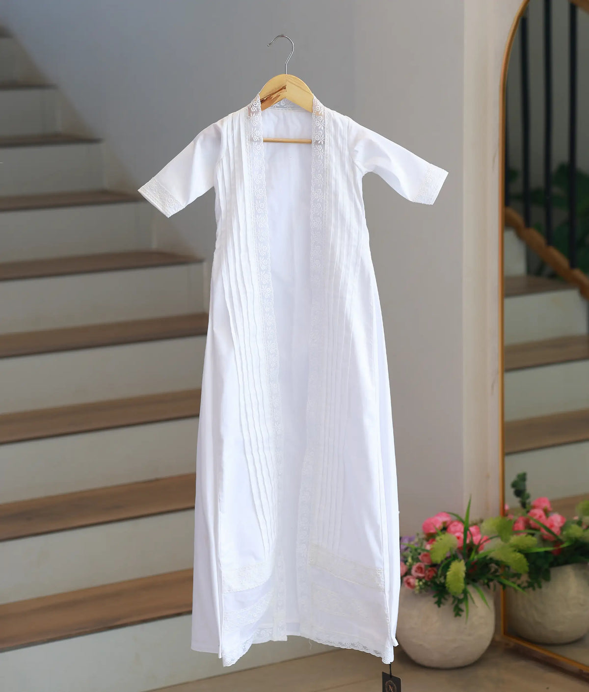 Full front view off white cotton baby baptism gown with an open-front floral lace overlayer hanging on hanger