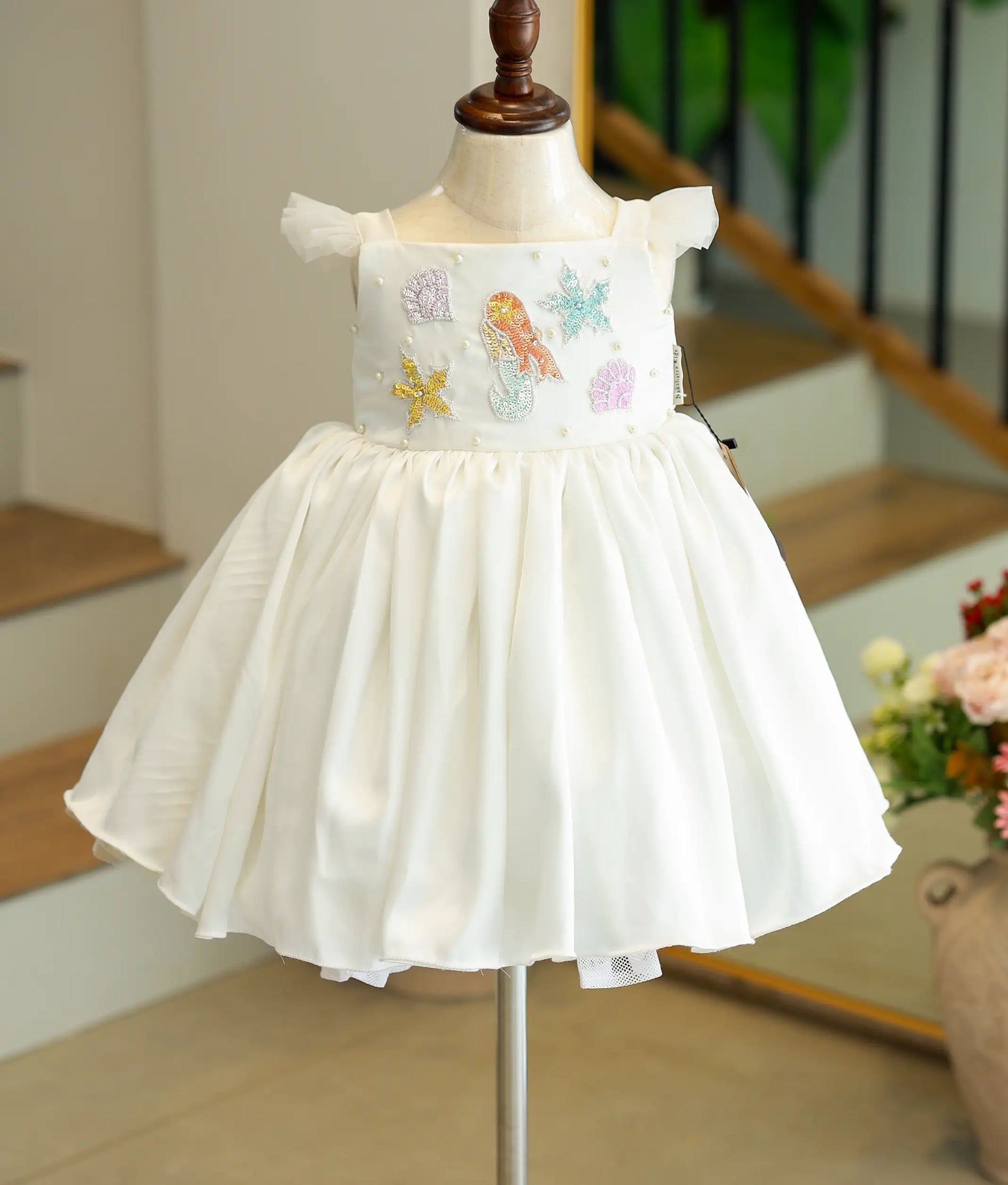 Front view of an white mermaid theme baby girl dress with a flared skirt and colorful applique details