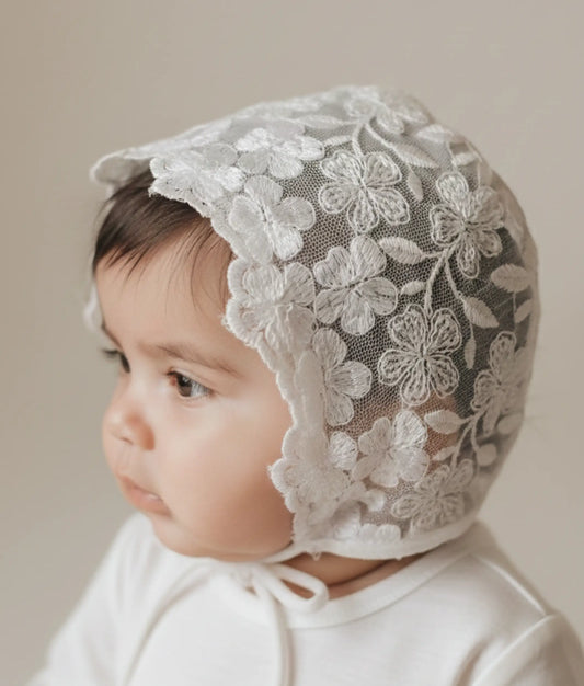 White floral lace baptism cap for baby girls featuring soft embroidered details and under-chin ties.