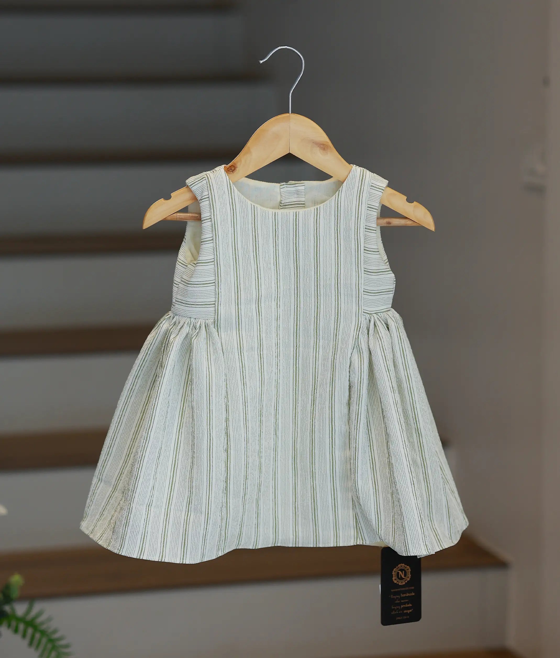 A front full-length view of a girls' sleeveless white frock with green vertical stripes and a gathered waist