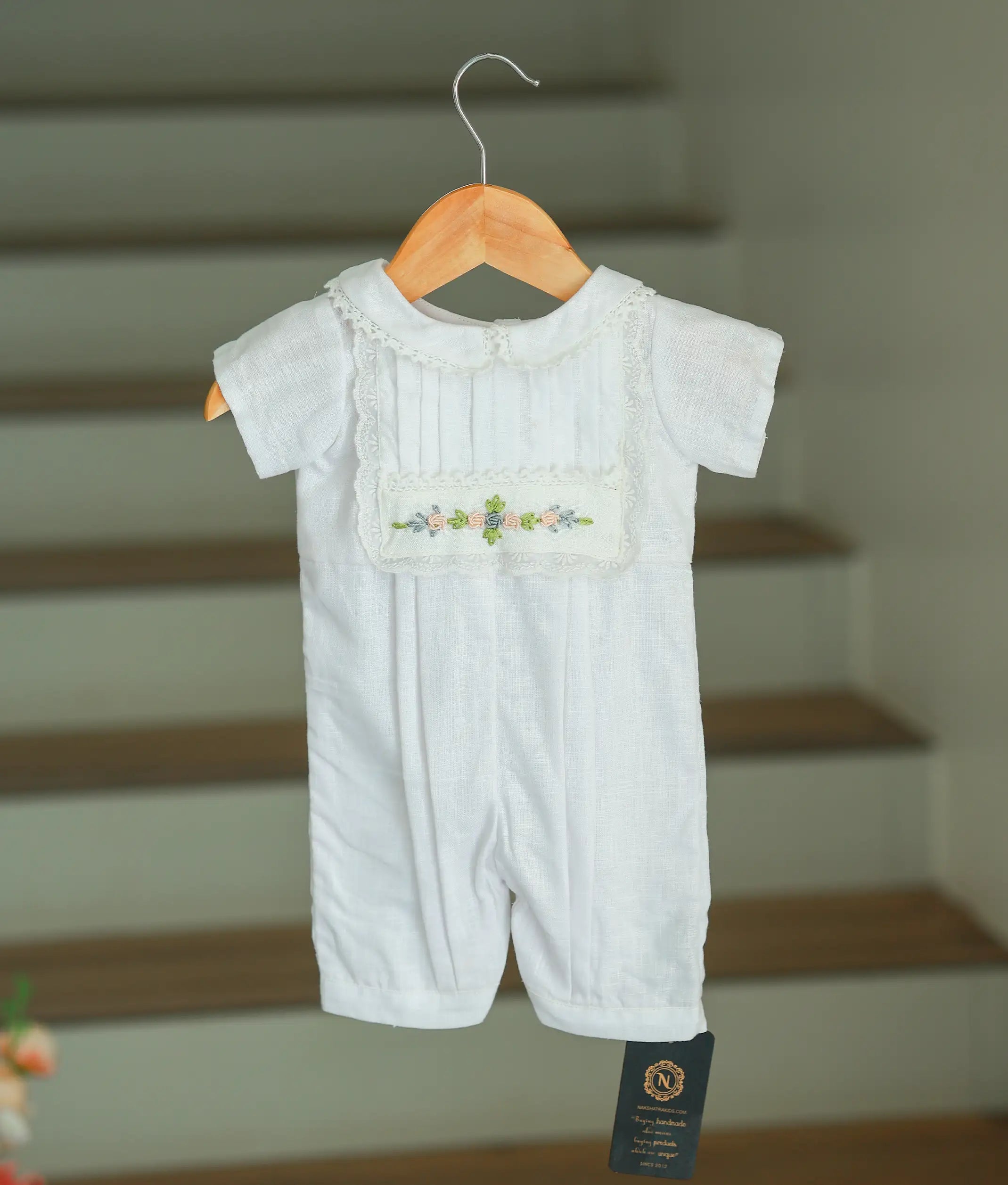 Front full-length view of a baby boy's white cotton baptism romper featuring a hand-embroidered floral chest panel and lace-trimmed collar