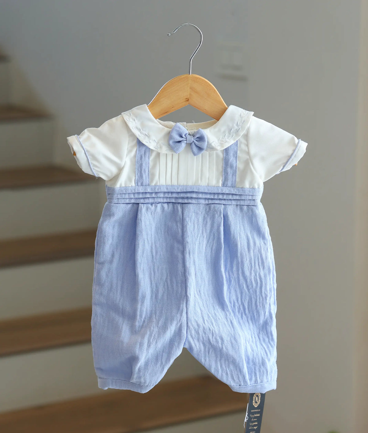 Front view of a white and light blue baby boy baptism romper with a bow tie and leaf embroidery.