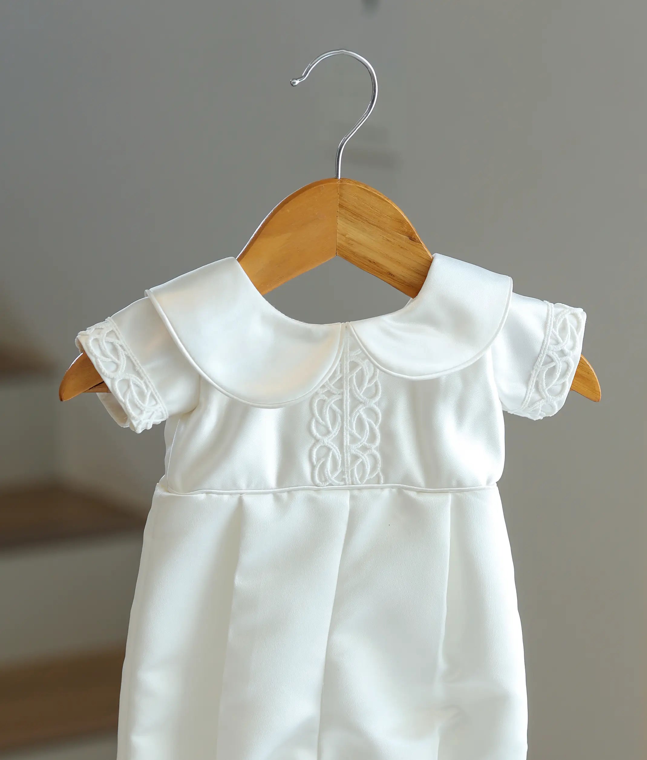 Close-up showing the embroidered knotwork on the chest and round Peter Pan collar of the satin romper.