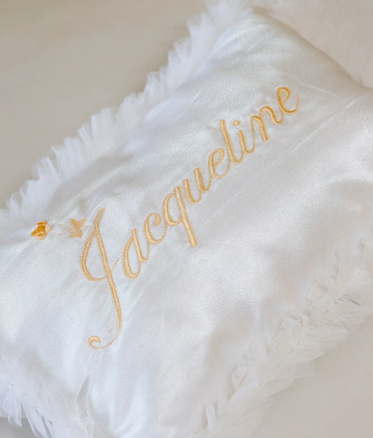Close-up of a white satin christening pillow featuring elegant tulle ruffles and personalized name detail.