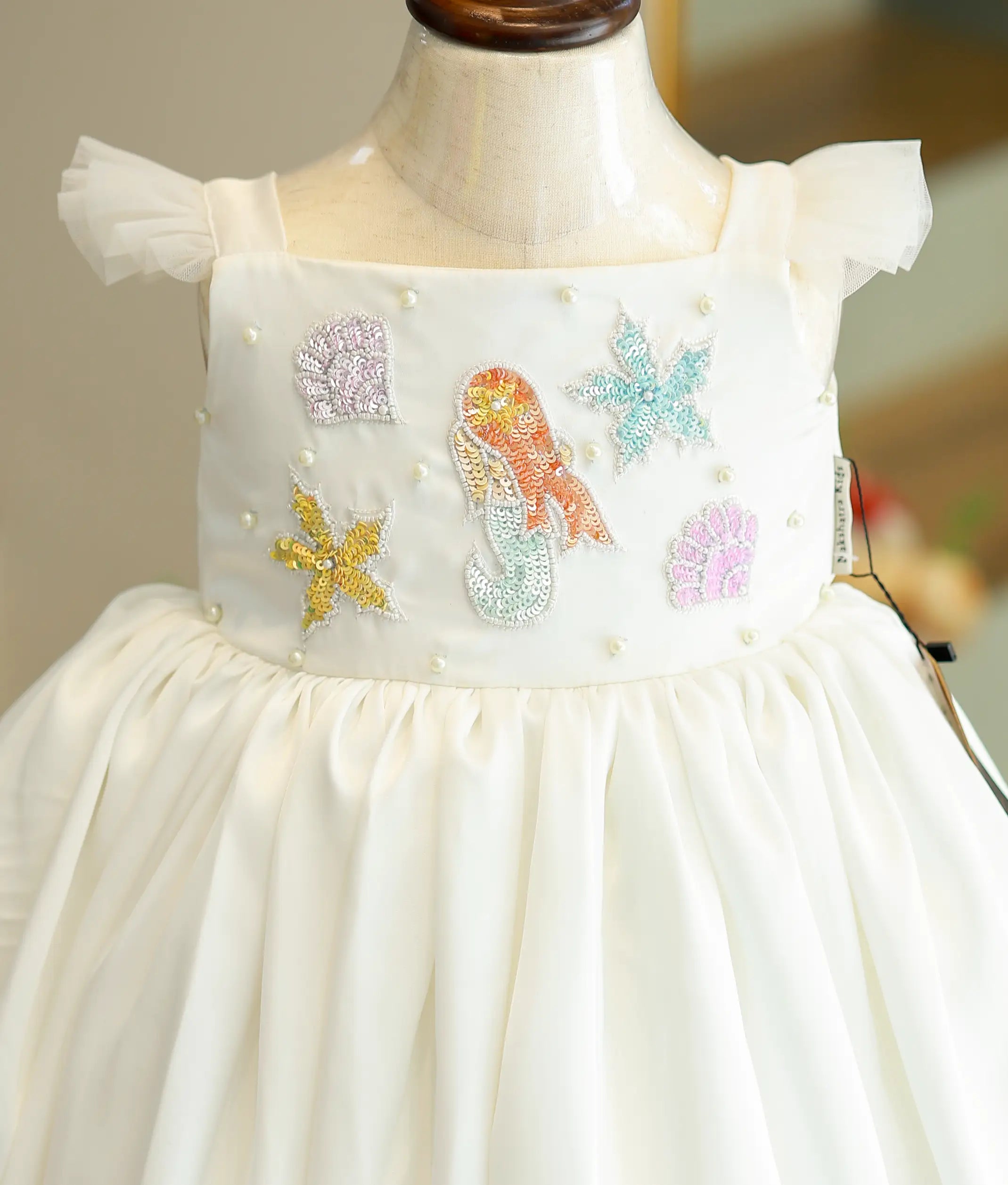 Close-up of the white satin dress bodice showing the mermaid embroidery and ruffled shoulder straps