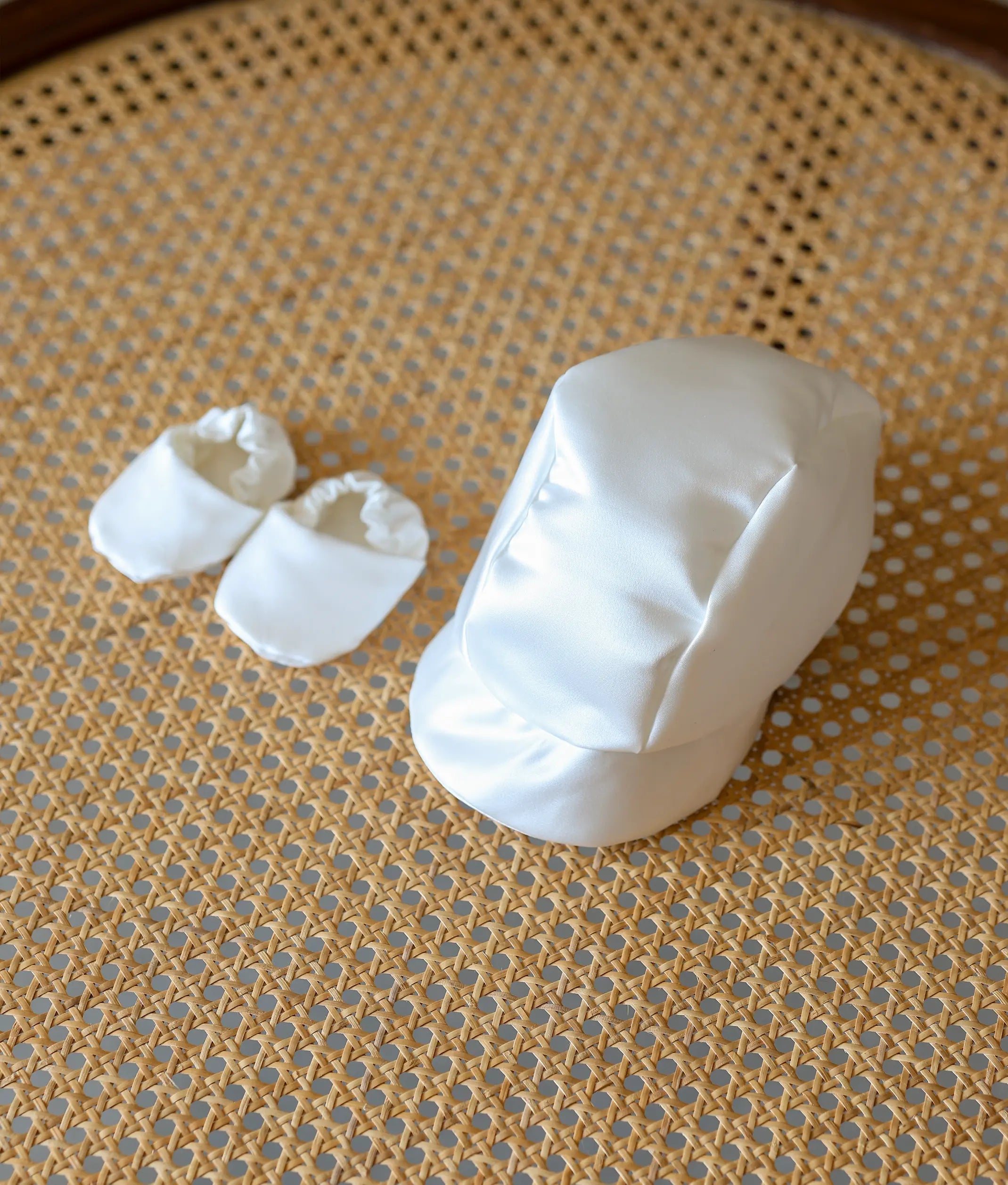 A matching white satin peaked cap and soft booties for a baby boy's baptism.