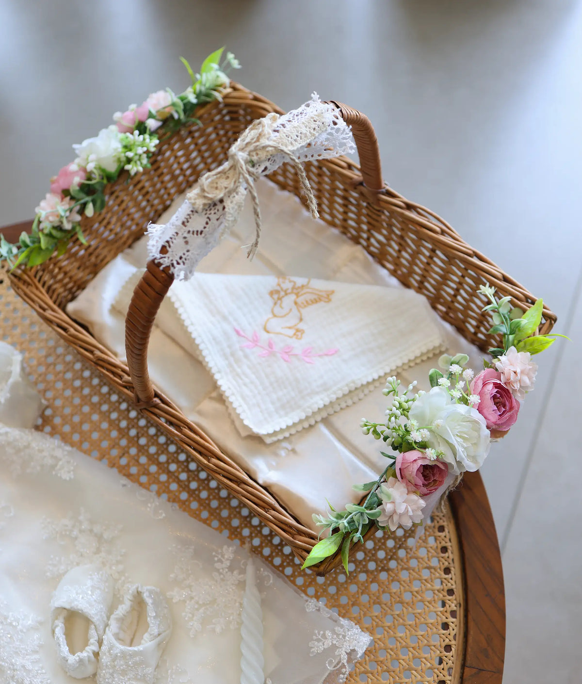 Woven baptism carrying basket trimmed with pink and white flowers, lace bow, and folded baptism towel.