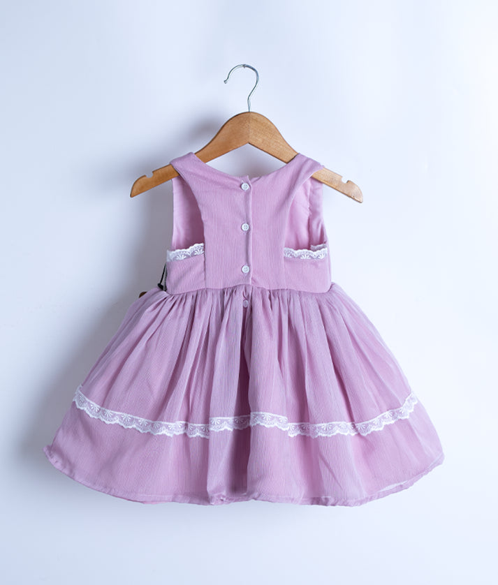 Back view of an baby pink sleeveless frock hanging on a hanger against a white background.