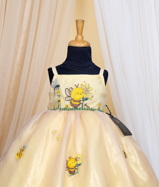 Close view of an golden dress with Honeybee theme on a mannequin against a beige curtain background.