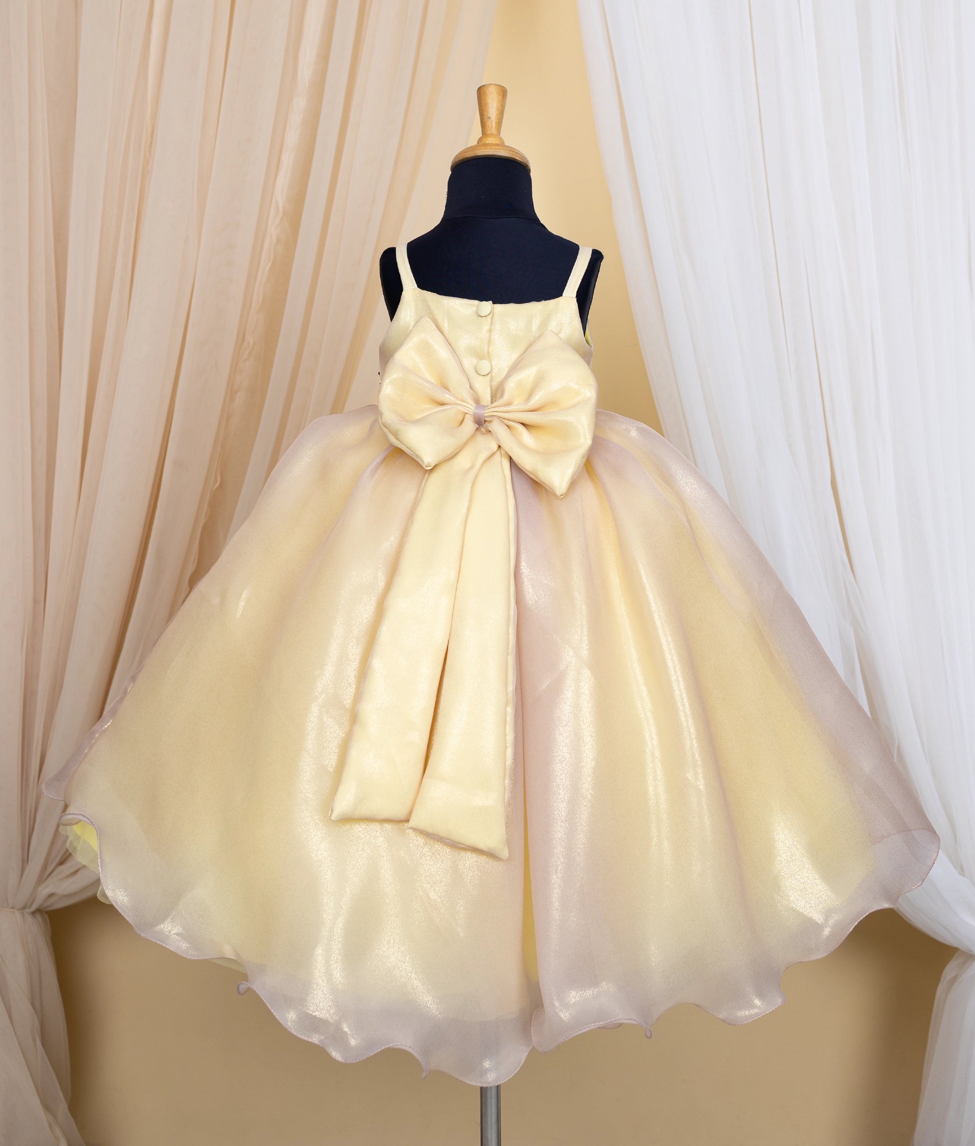 Back view of an golden dress with honeybee theme on a mannequin against a beige curtain background.