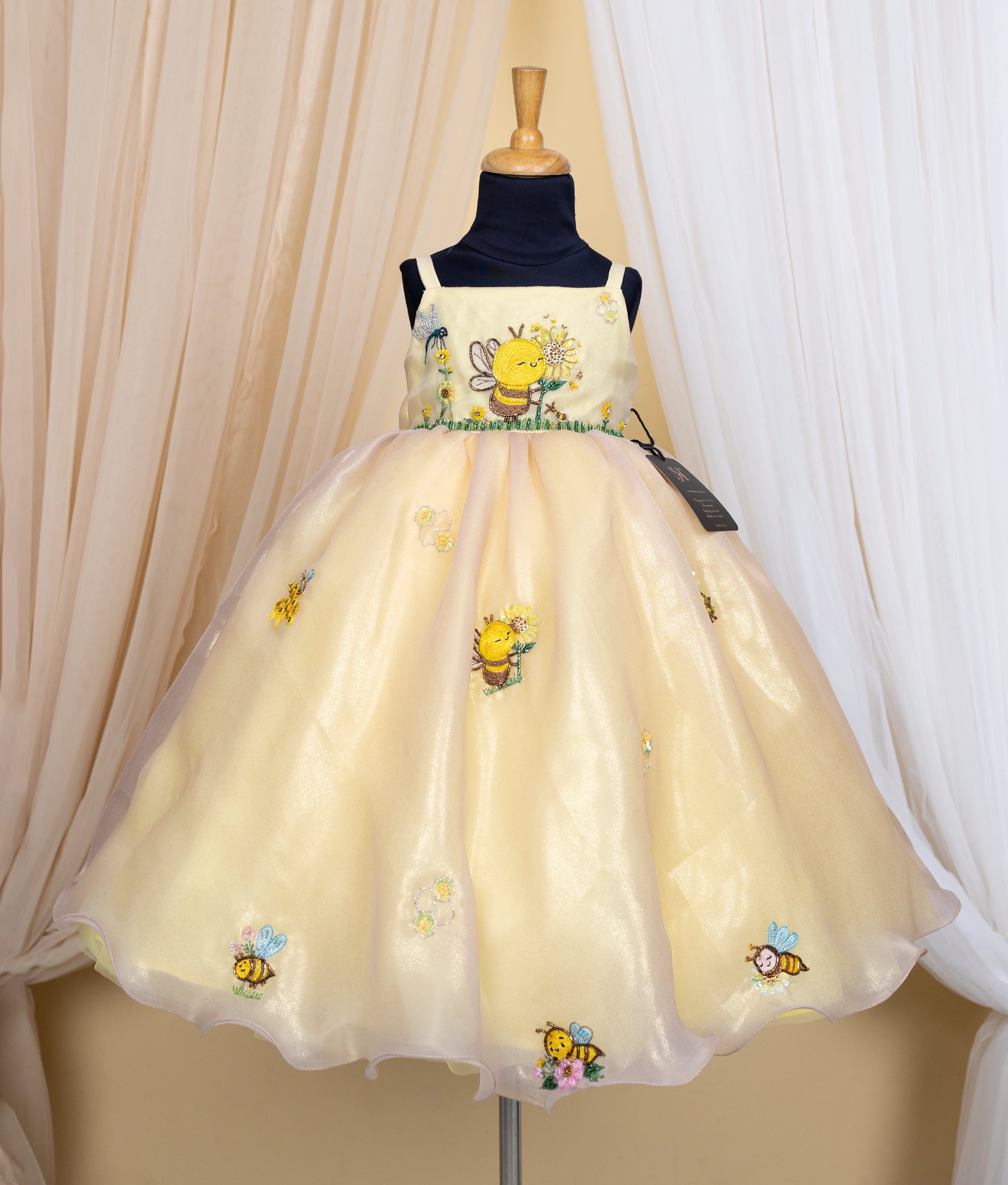 Golden dress with honeybee theme on a mannequin against a beige curtain background.