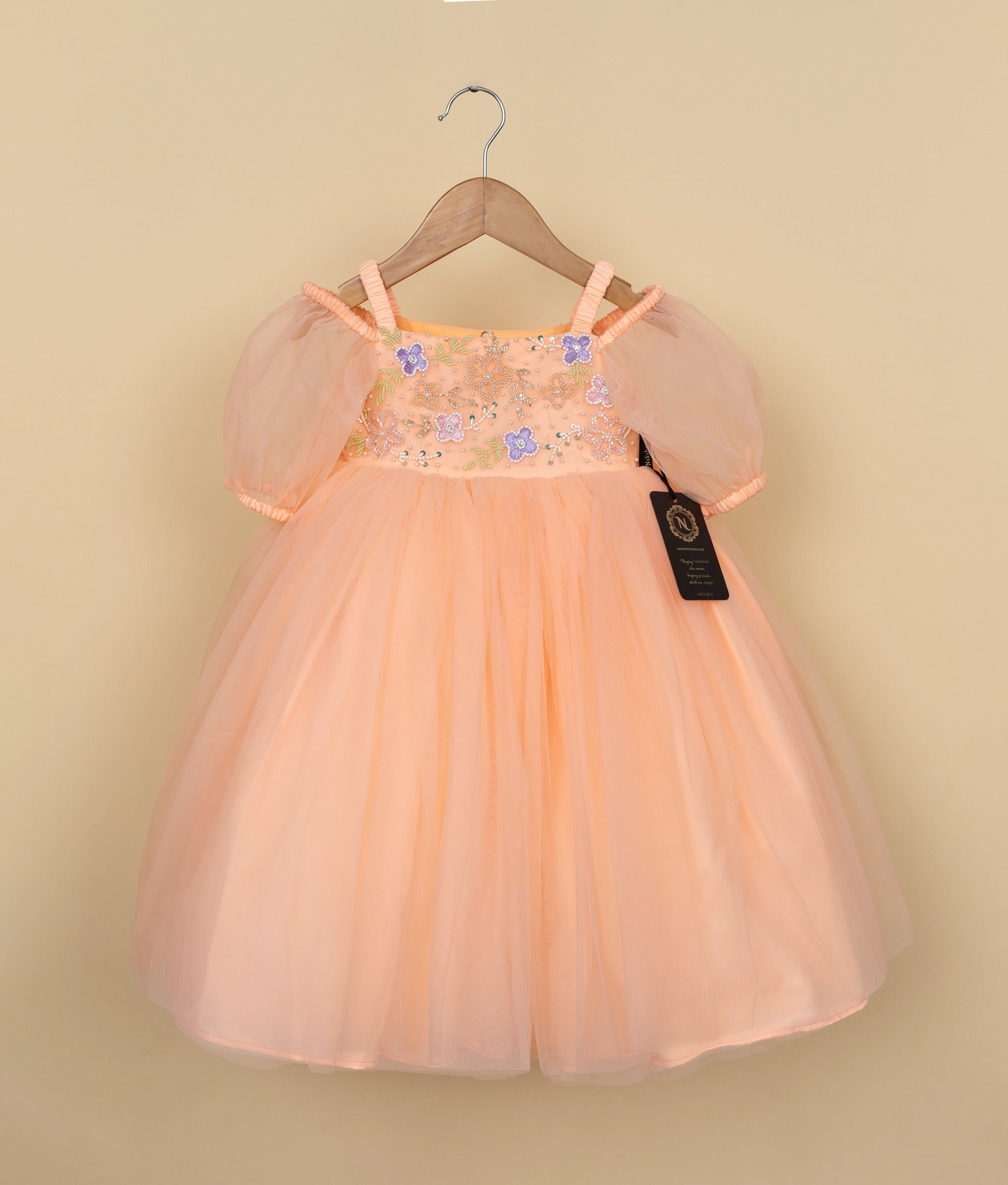 Peach-colored dress with floral embellishments on a hanger against a beige background.