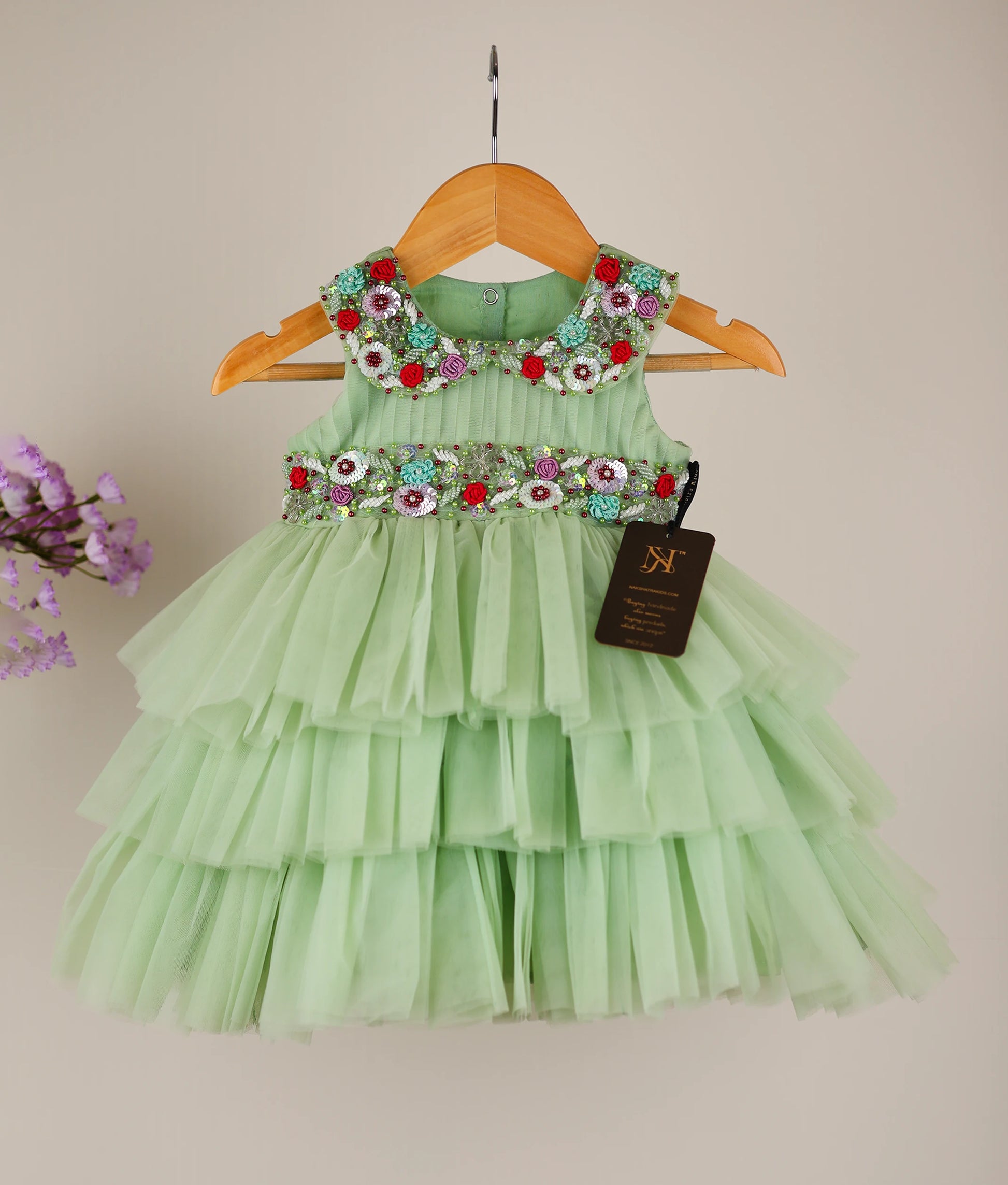Front view of pastel green tulle net handworked birthday dress against plain background