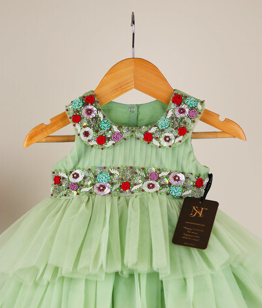 Close view of pastel green tulle net handworked birthday dress against plain background