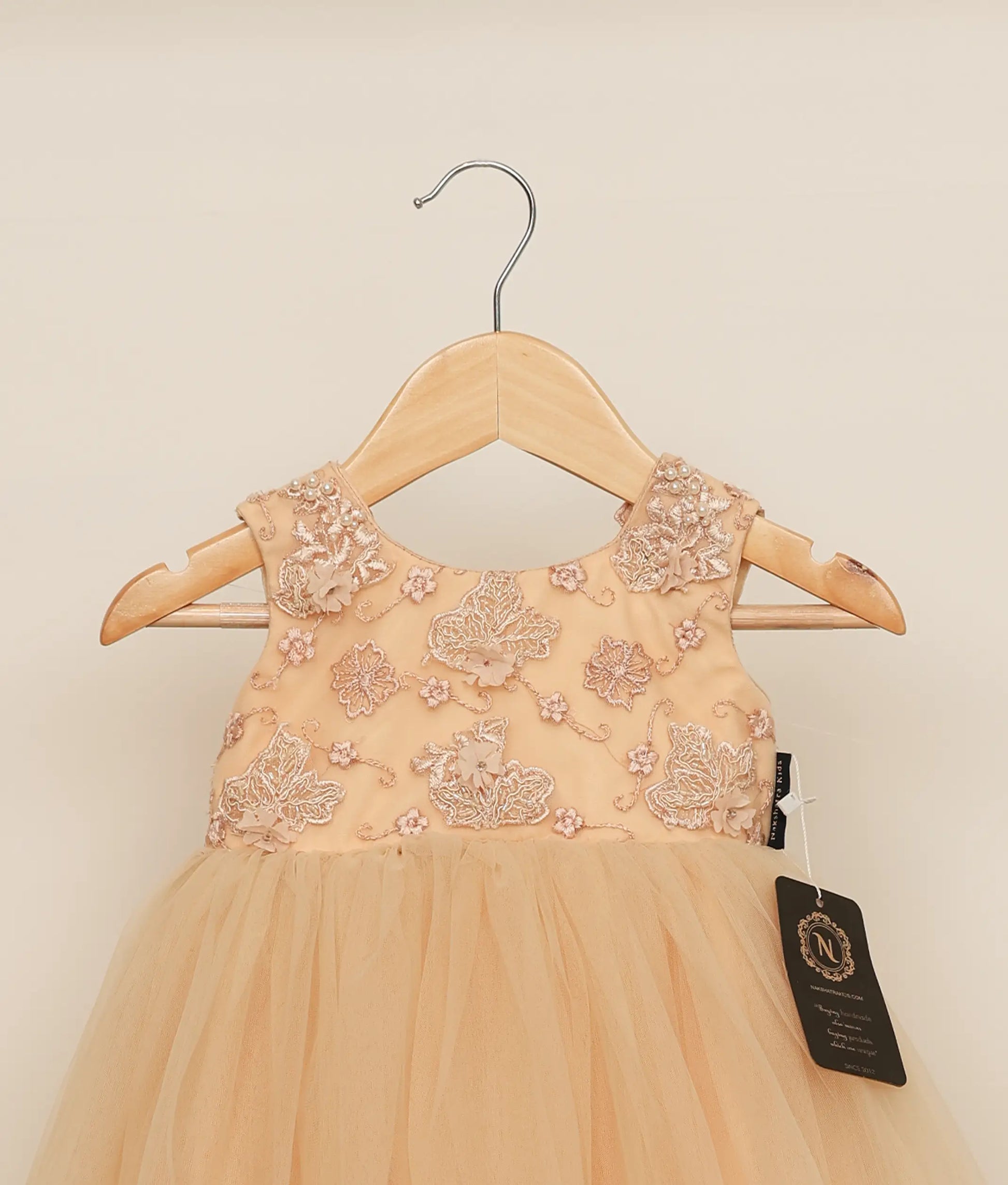Close view of golden tulle net appliqué frock for baby girl against plain background 