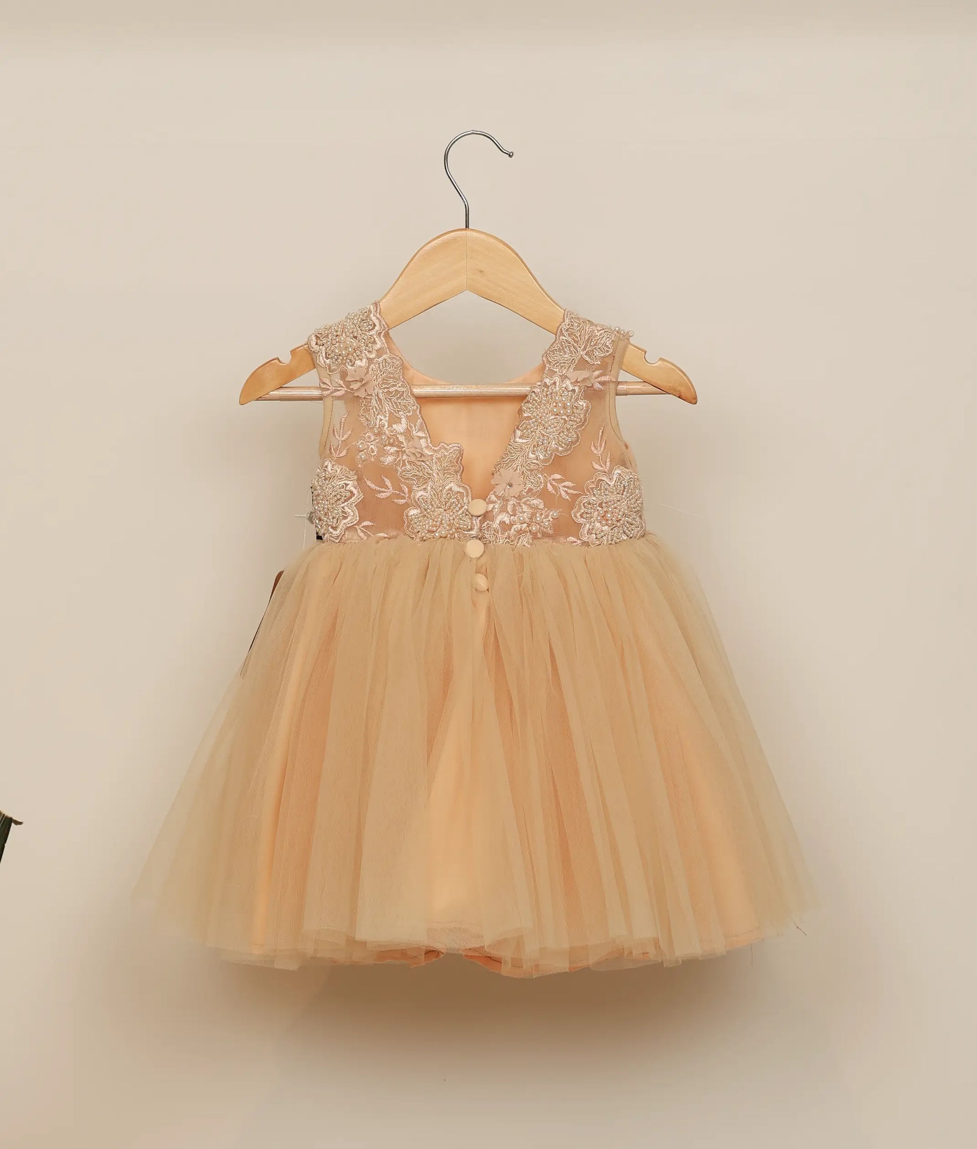 Back view of golden tulle net appliqué frock for baby girl against plain background 