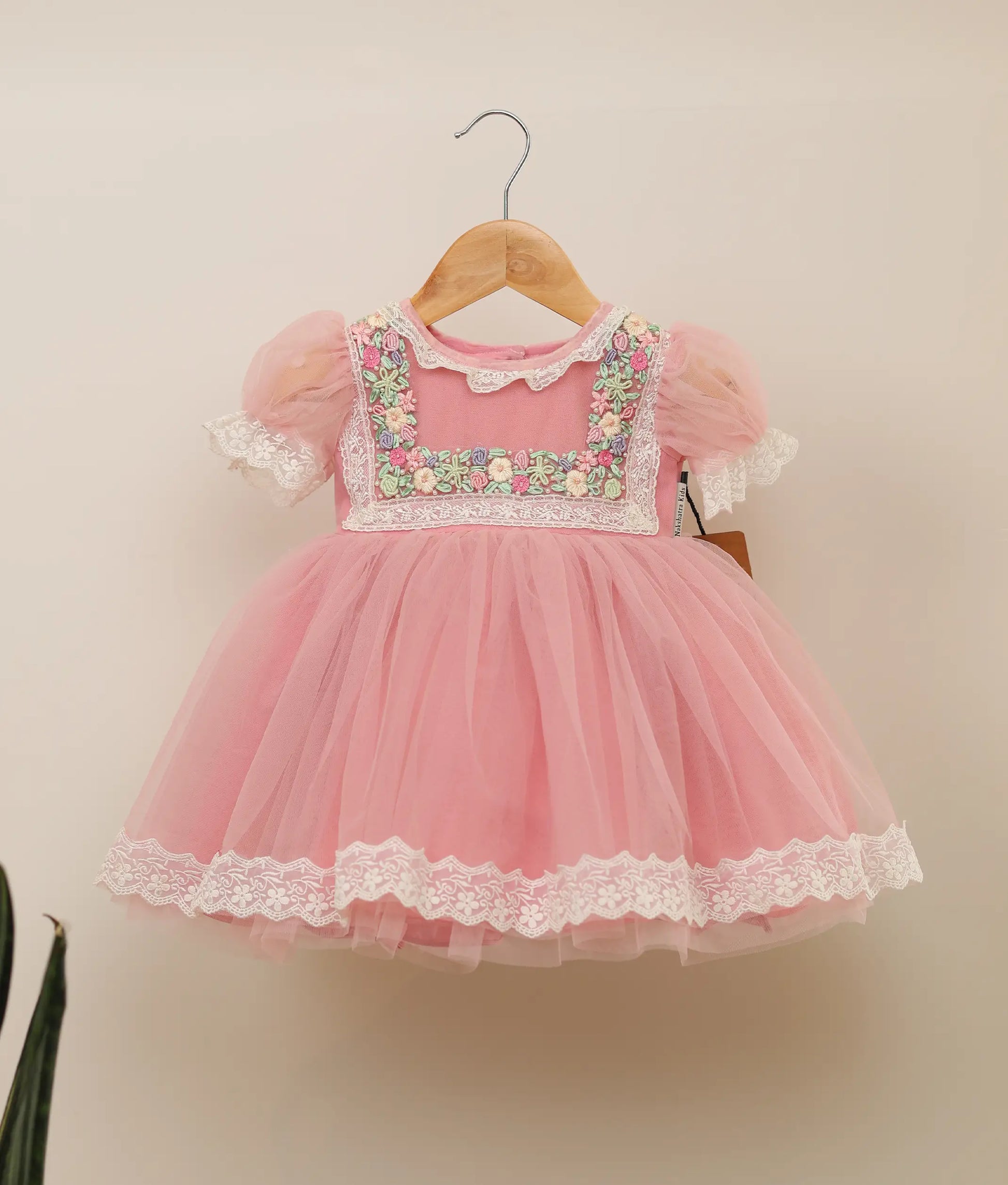 Front view of pink tulle net handworked birthday frock against plain background 