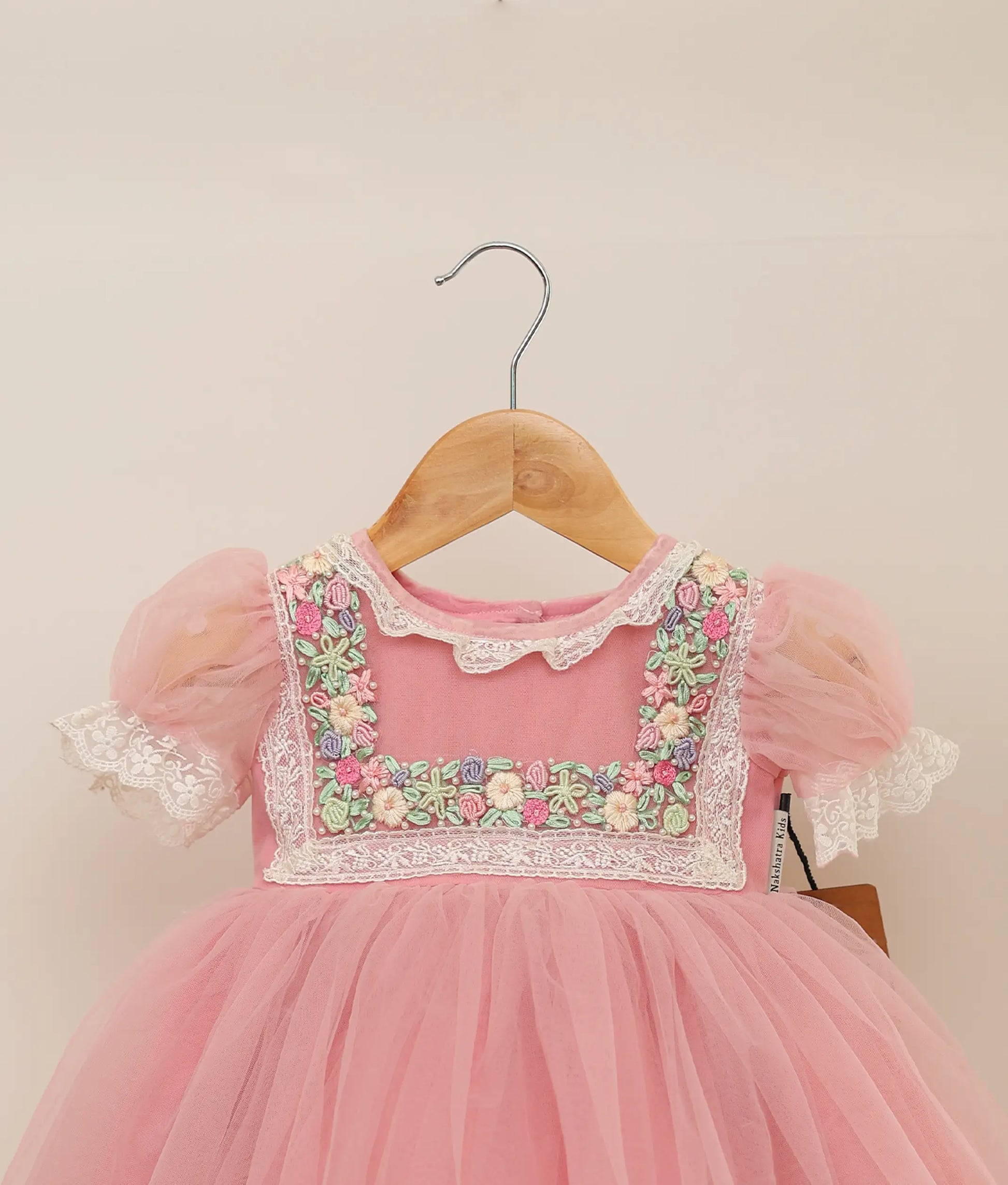 Close view of pink tulle net handworked birthday frock against plain background 