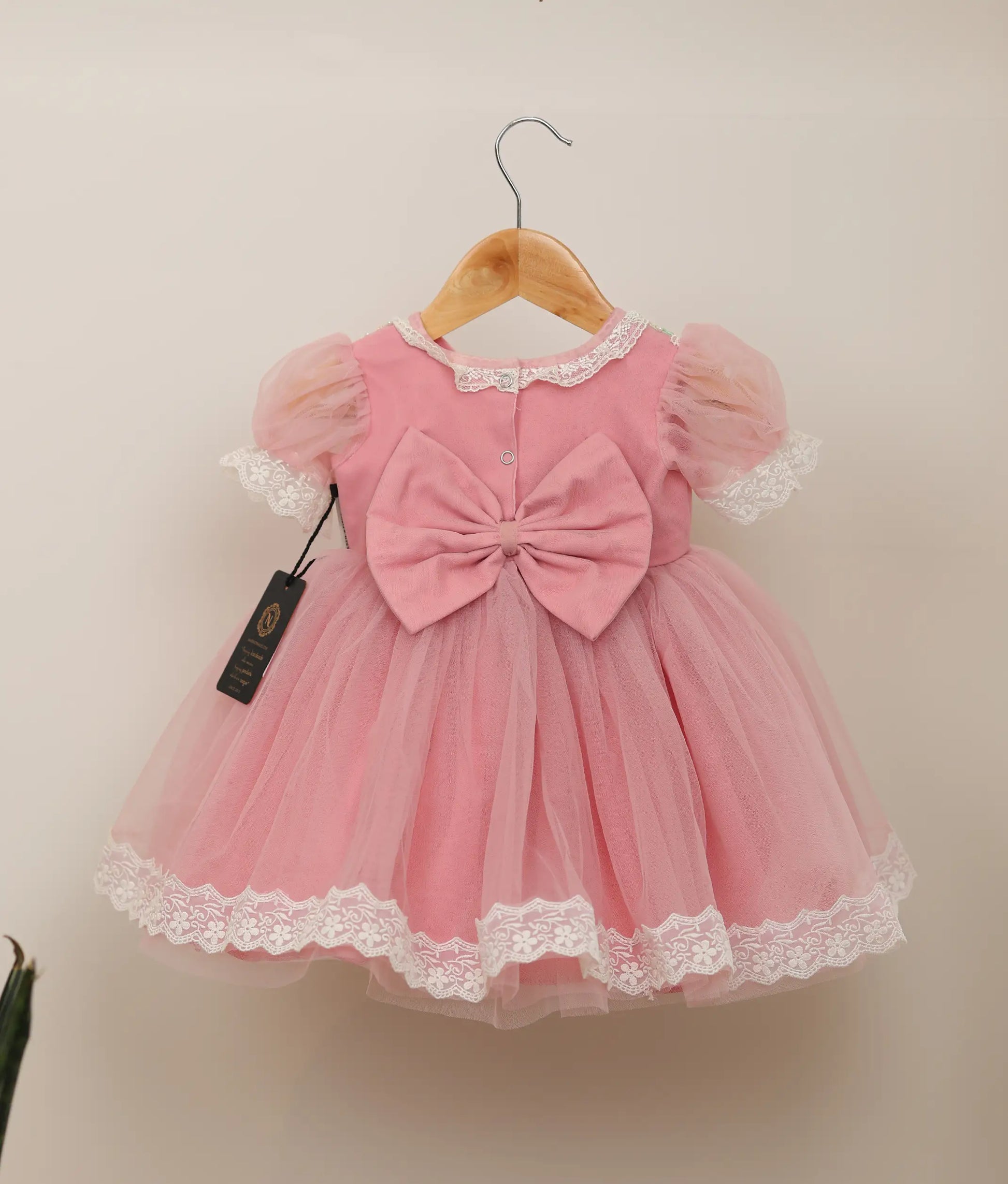 Back view of pink tulle net handworked birthday frock against plain background 