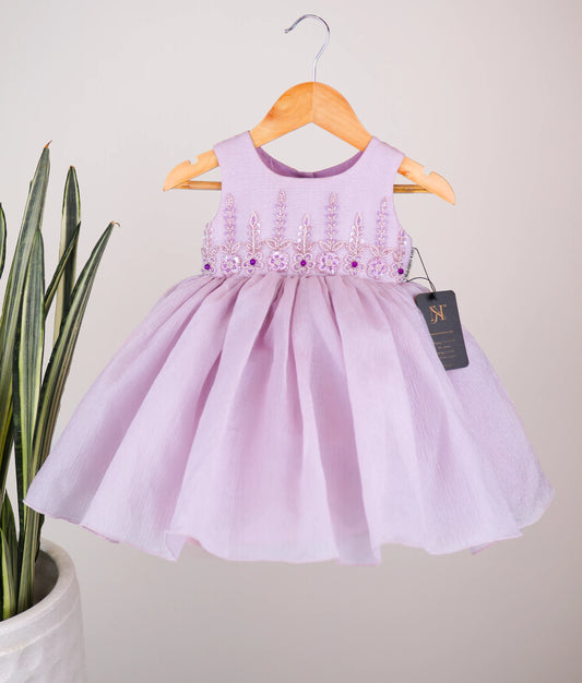 Pastel lavender frock with floral embroidery on a hanger against a light background.