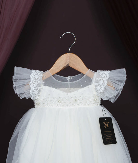 Close view of an off-white baby girl baptism dress with lace, pearls, and frilled sleeves on a hanger.