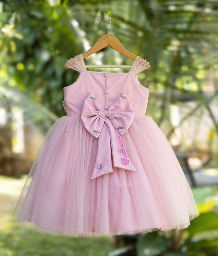 Back view of pink baby girl frock with large decorative bow, tulle skirt, and sheer polka dot straps – elegant outfit for birthdays and special occasions.