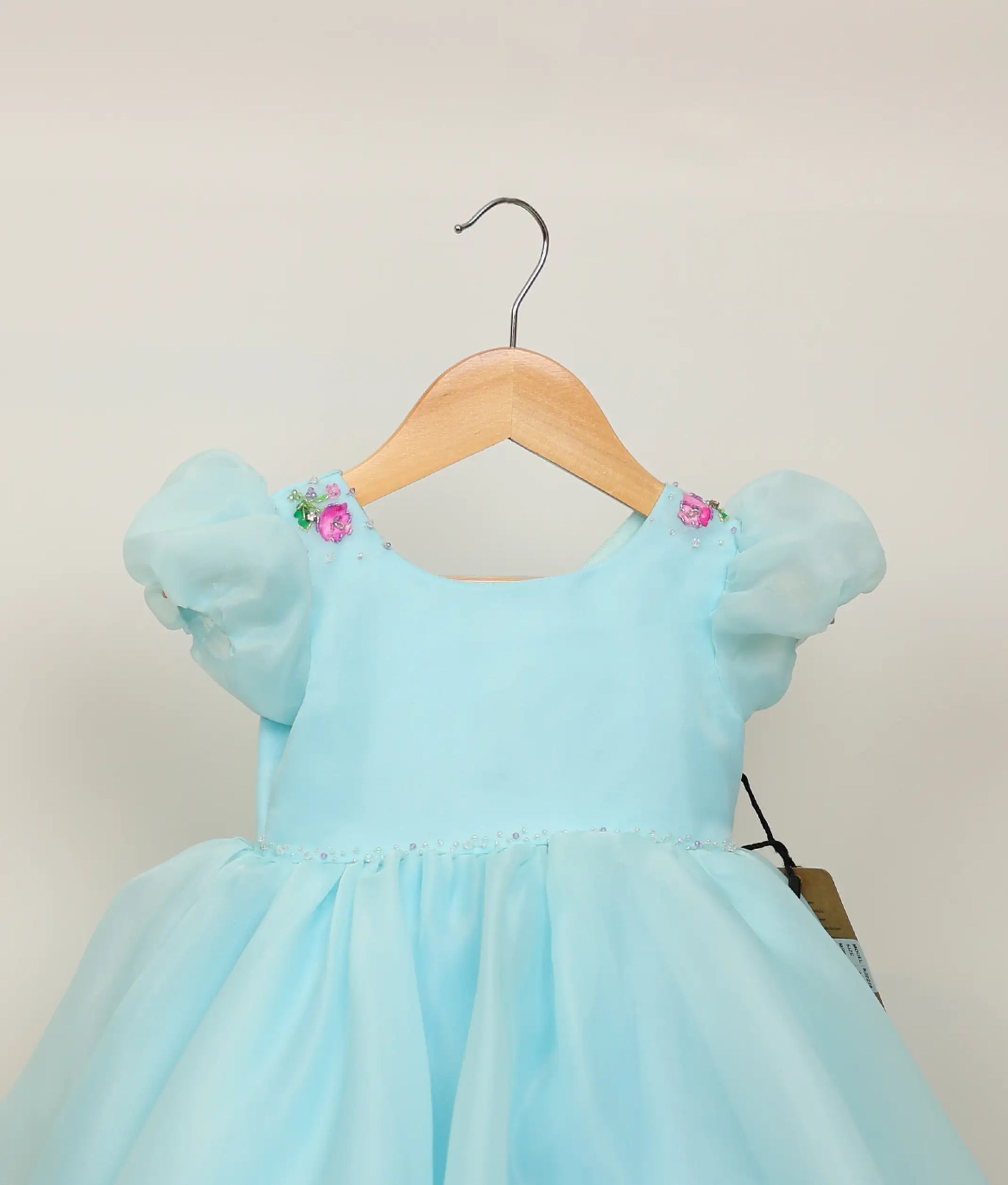 Close view of sky blue plain organza floral painting and handworked birthday gown against plain background