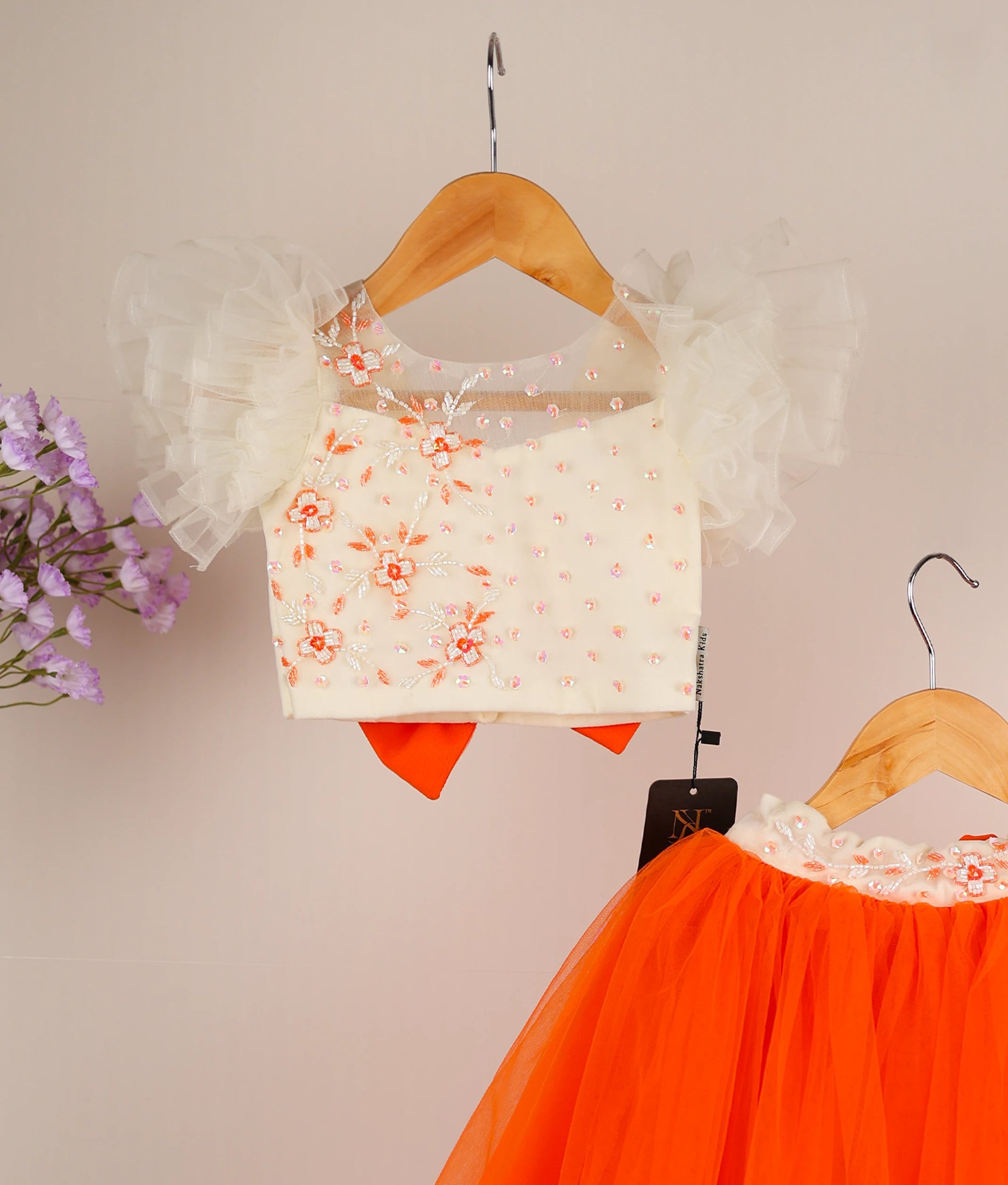Close view of an off-white handworked butterfly sleeve with orange full-length skirt against a plain background