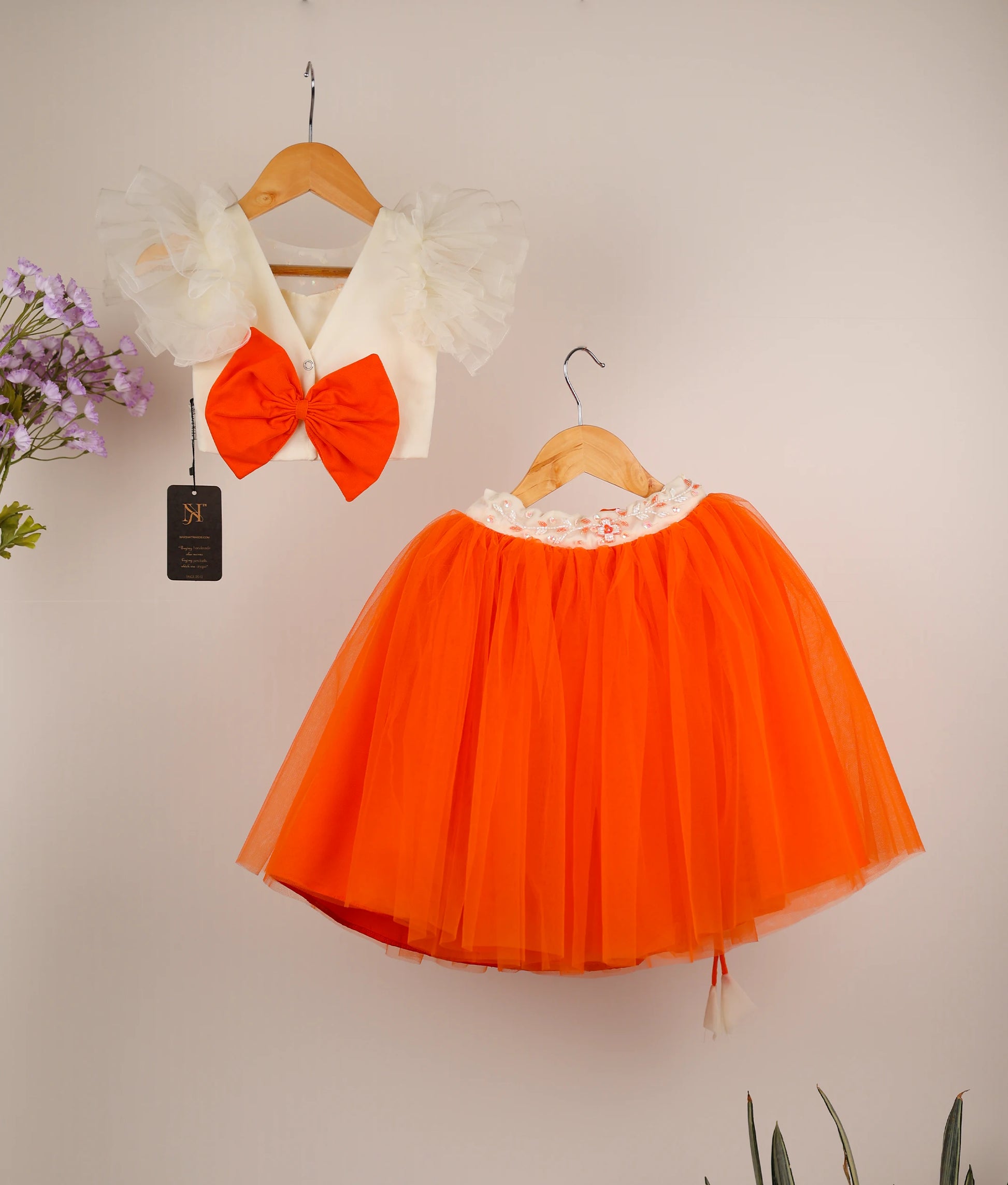 Back view of an off-white handworked butterfly sleeve with orange full-length skirt against a plain background
